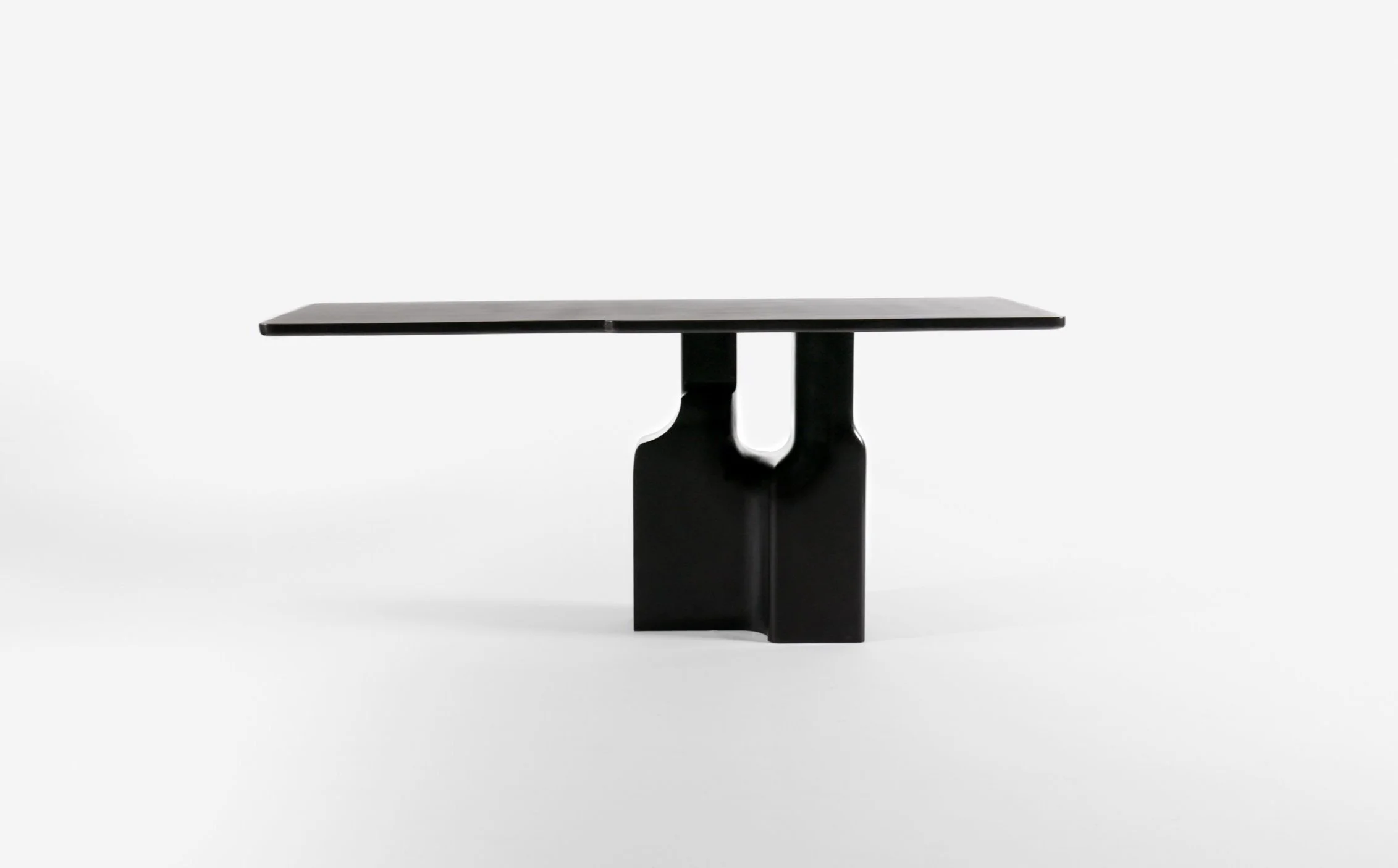 Black modern dining table with a flat rectangular top and sculptural base, set against a plain white background.