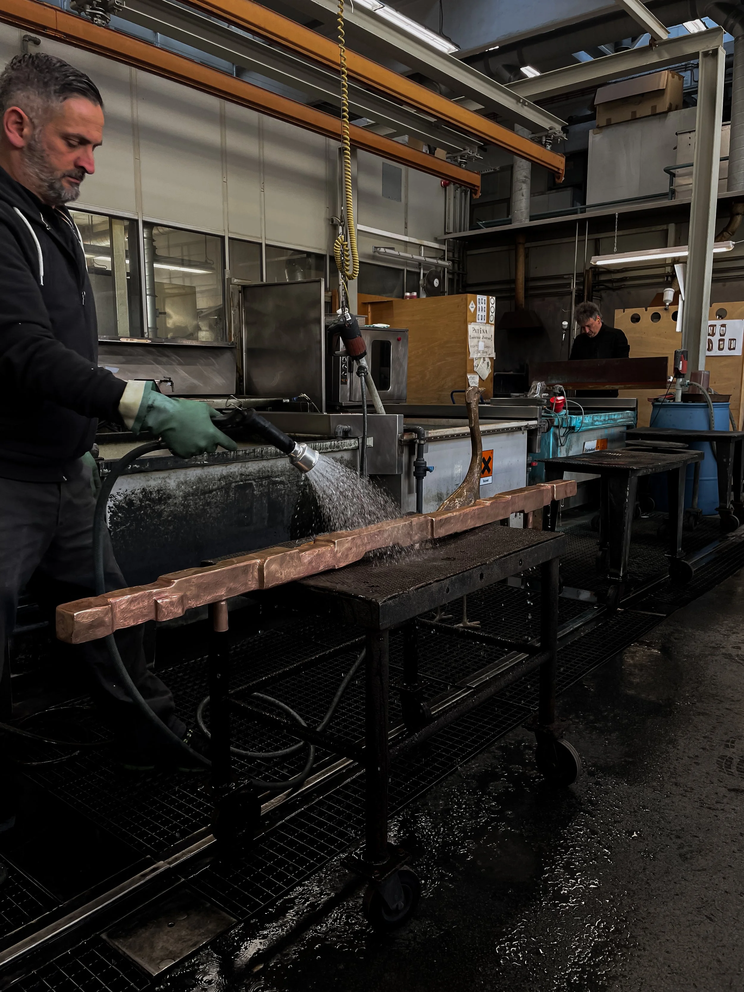 Man in black hoodie and gloves welding from a water-cooling station in an industrial workshop.