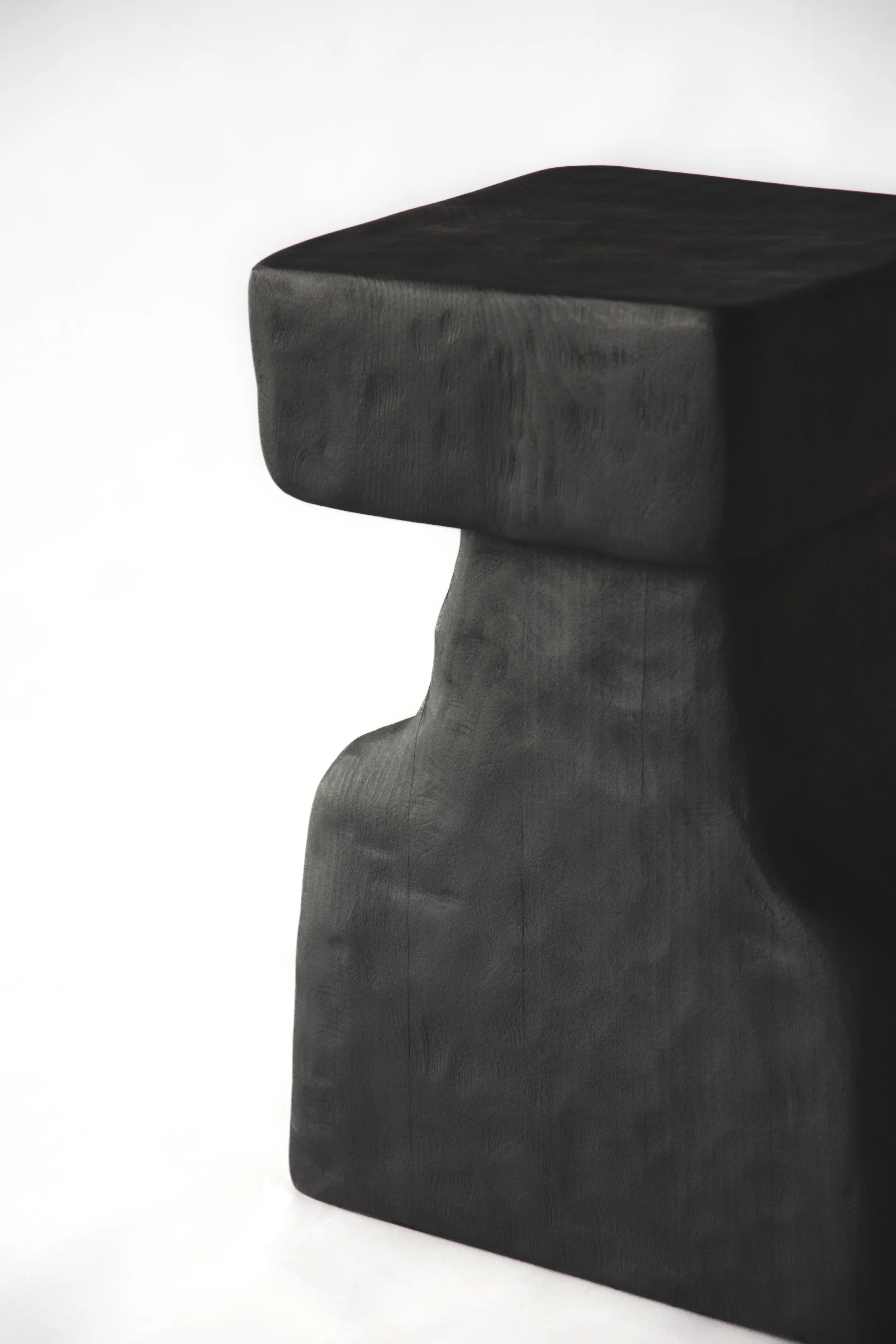 Close-up of a black wooden sculpture with a geometric, abstract form, placed against a plain white background.
