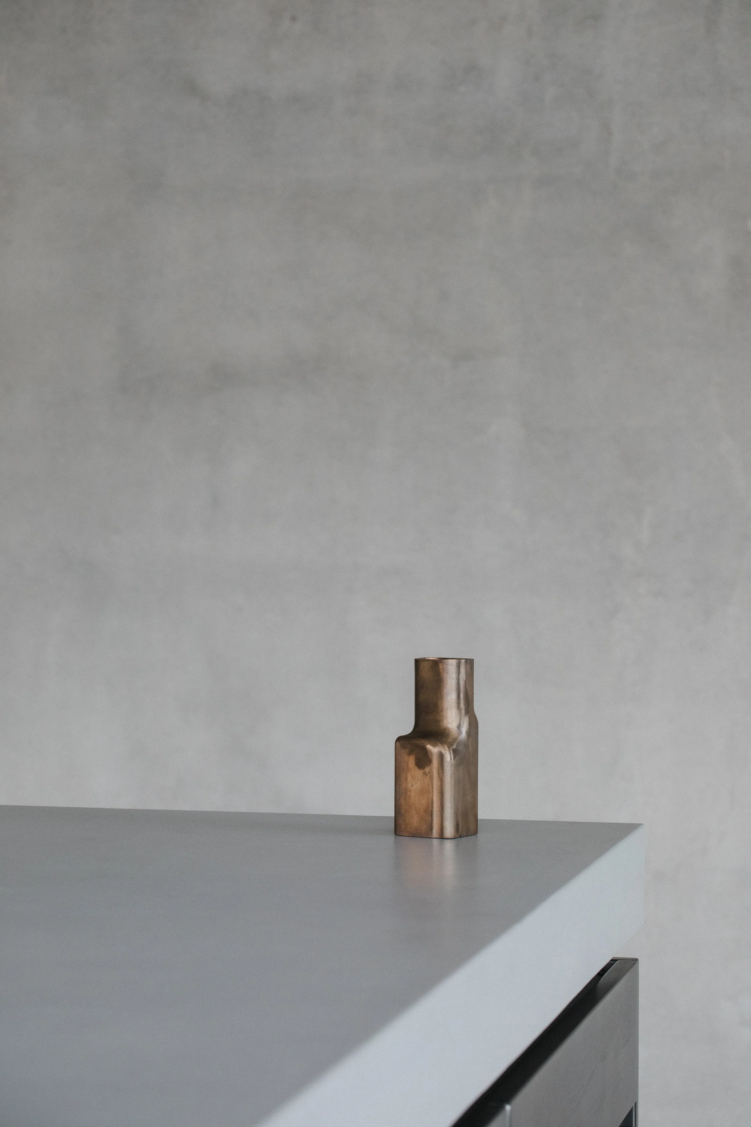 A small, metallic sculpture placed on a white table against a gray textured wall.