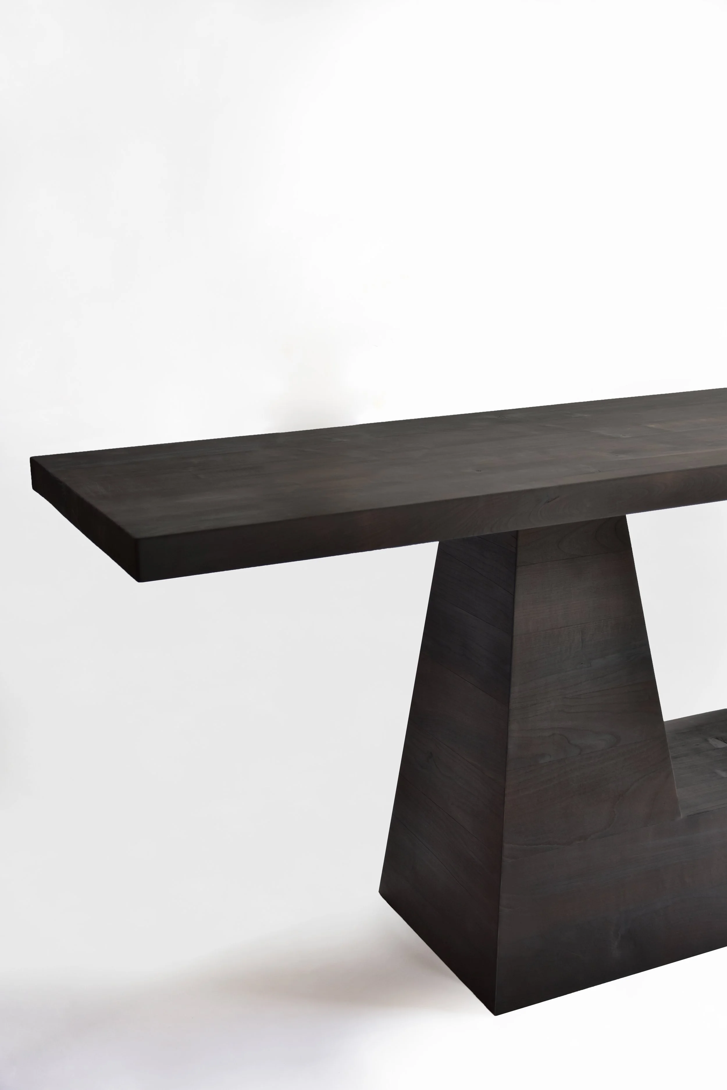 Close-up of a modern, dark wooden table with a geometric base against a white background.