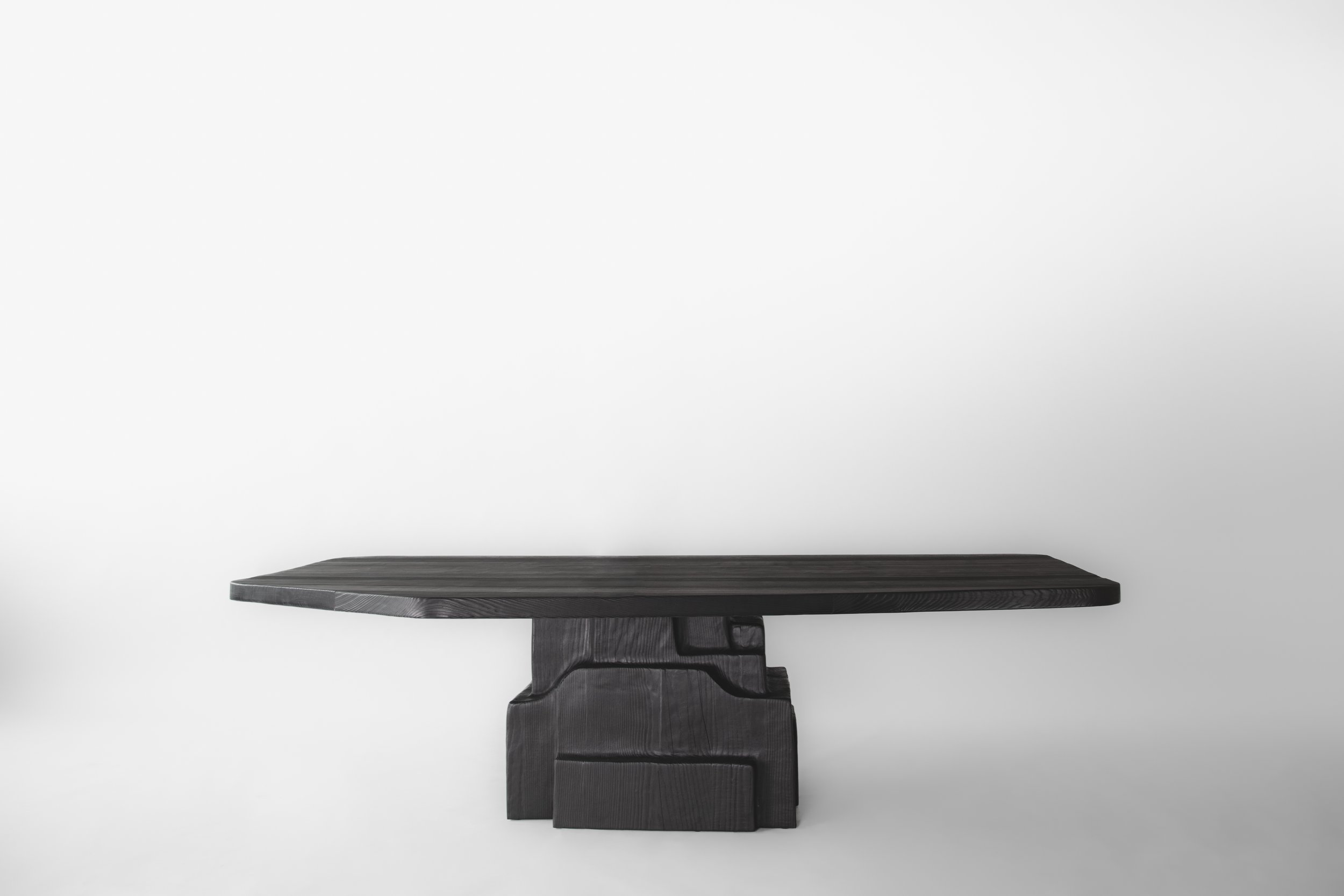 Dark wood table with a thick top and a base made of stacked, carved wood pieces, set against a plain white background.