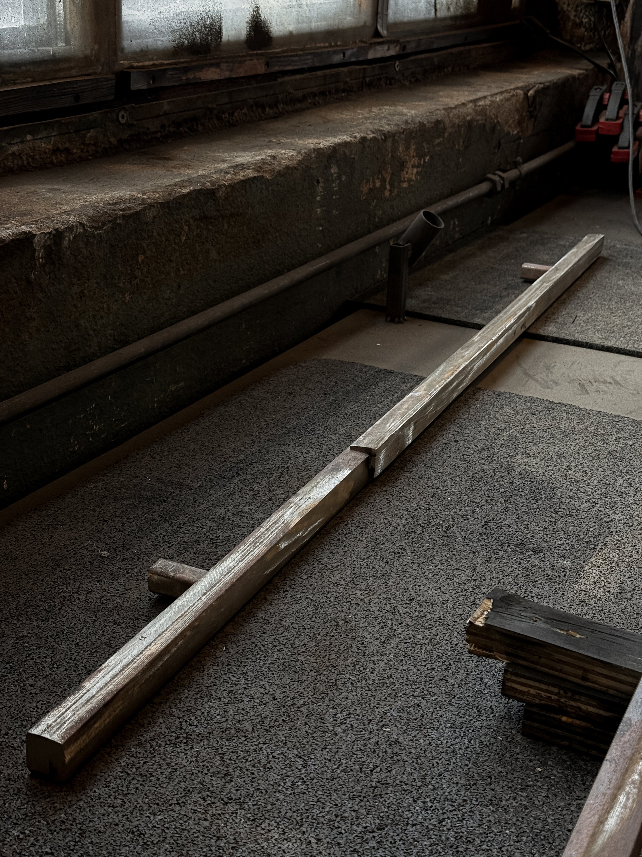 Wooden board and metal rod on an industrial floor with black safety matting.