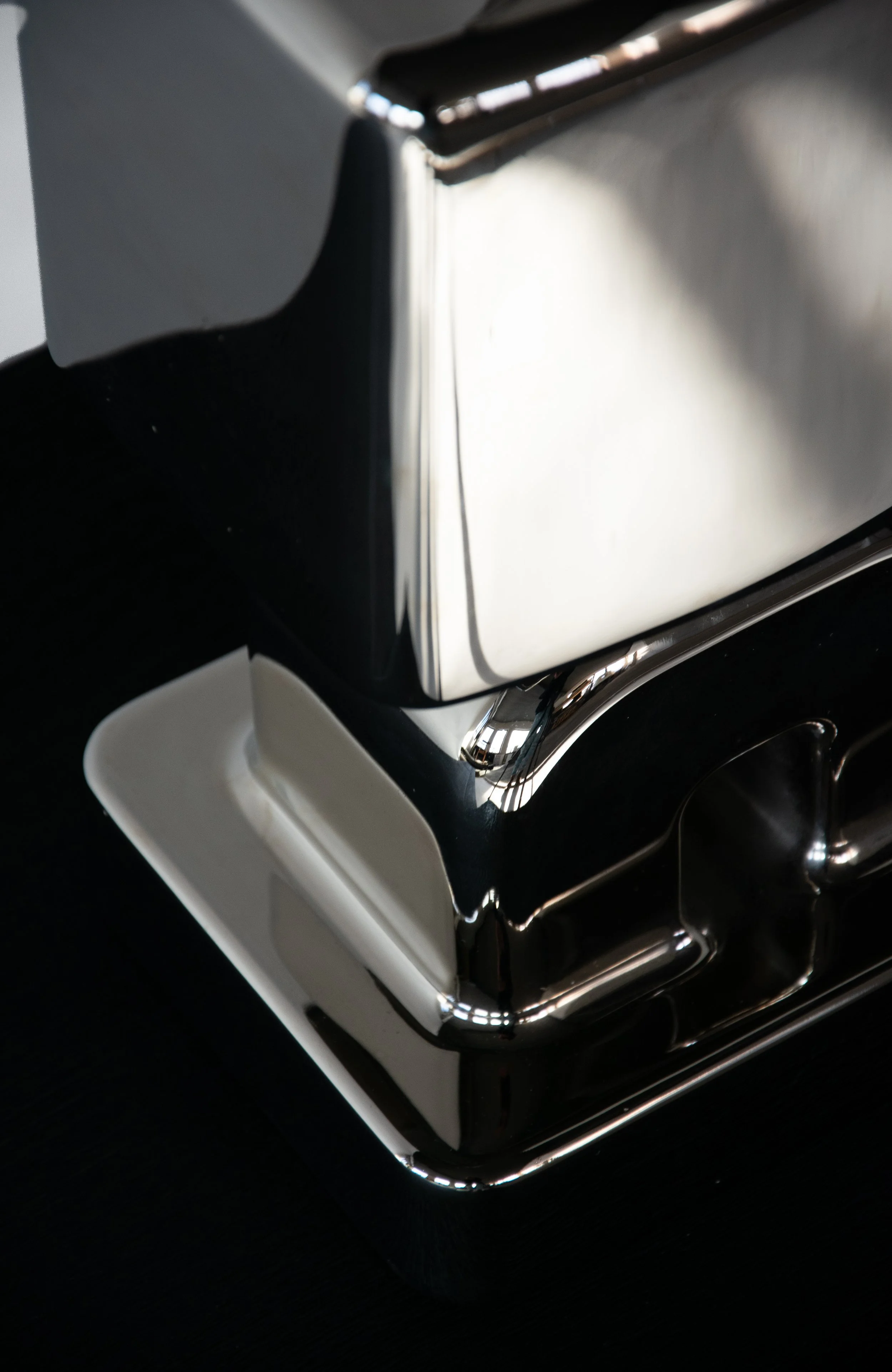 Close-up of a shiny, reflective silver and black object, possibly a vintage or decorative item, with a focus on its corner and edges.