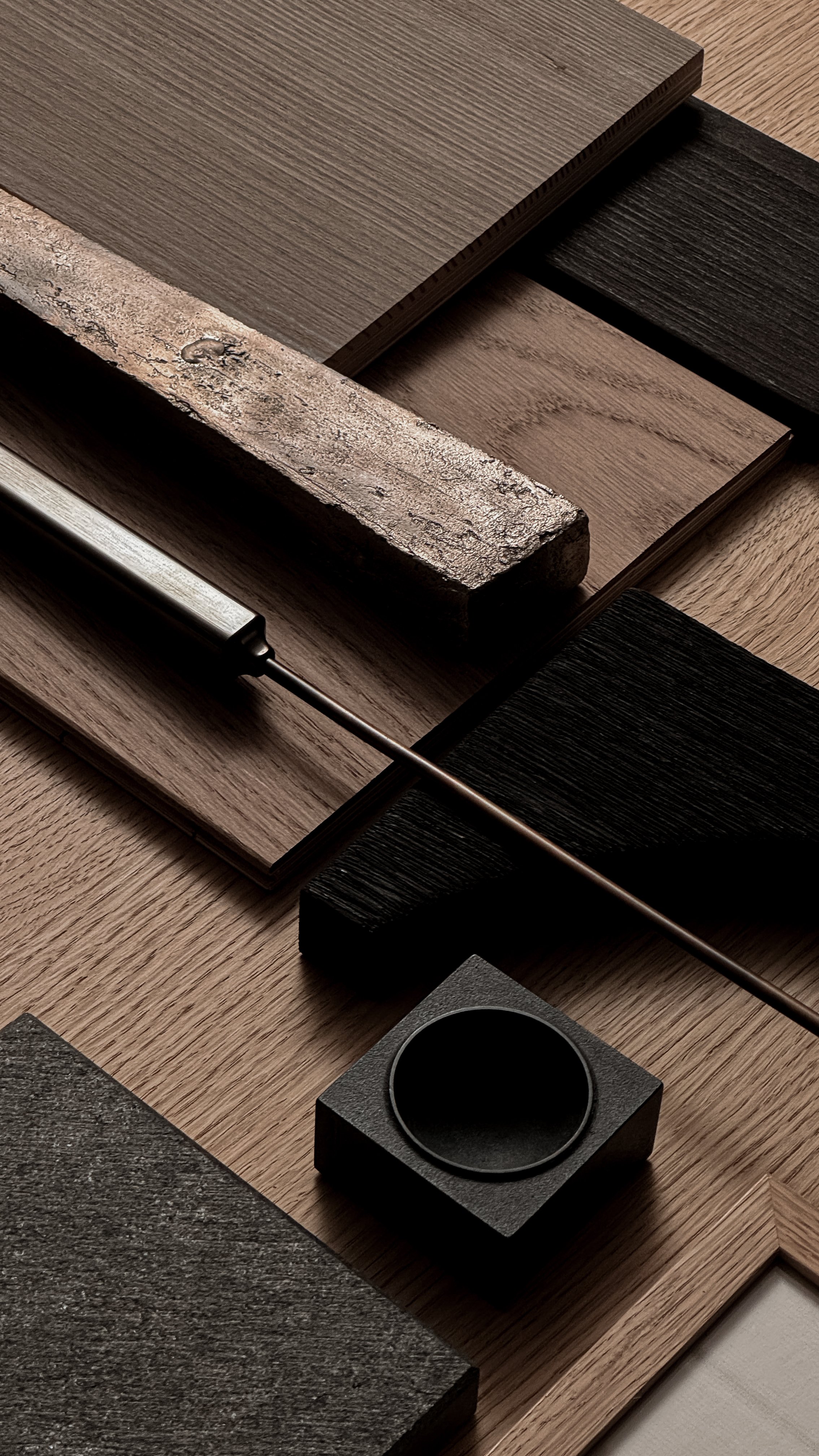 Various wood and material samples arranged on a surface, including different textures and colors of wood, a metal tool, and a black circular object.