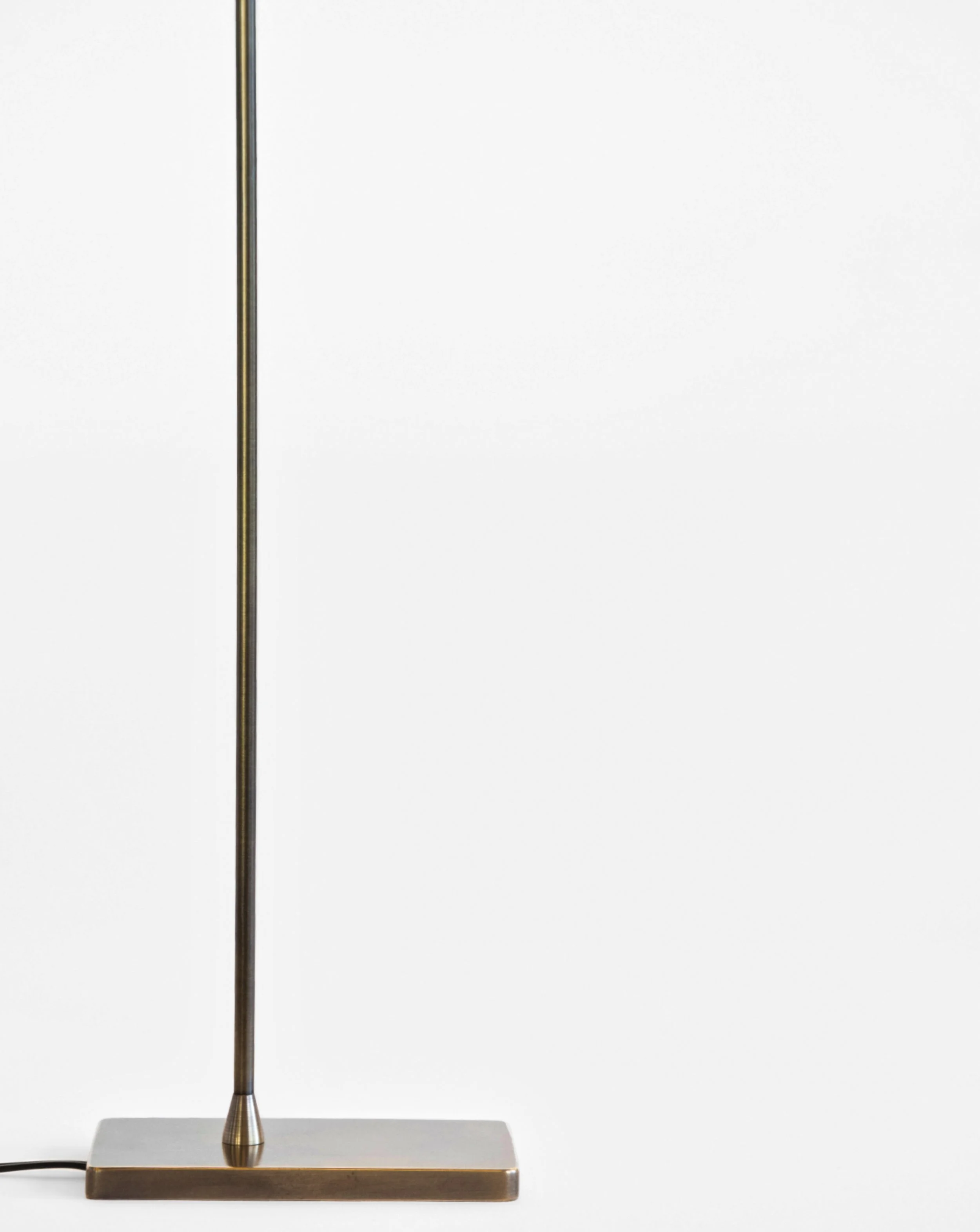Close-up view of a modern, metallic desk lamp with a rectangular base and a tall, slender vertical arm, placed against a plain white background.