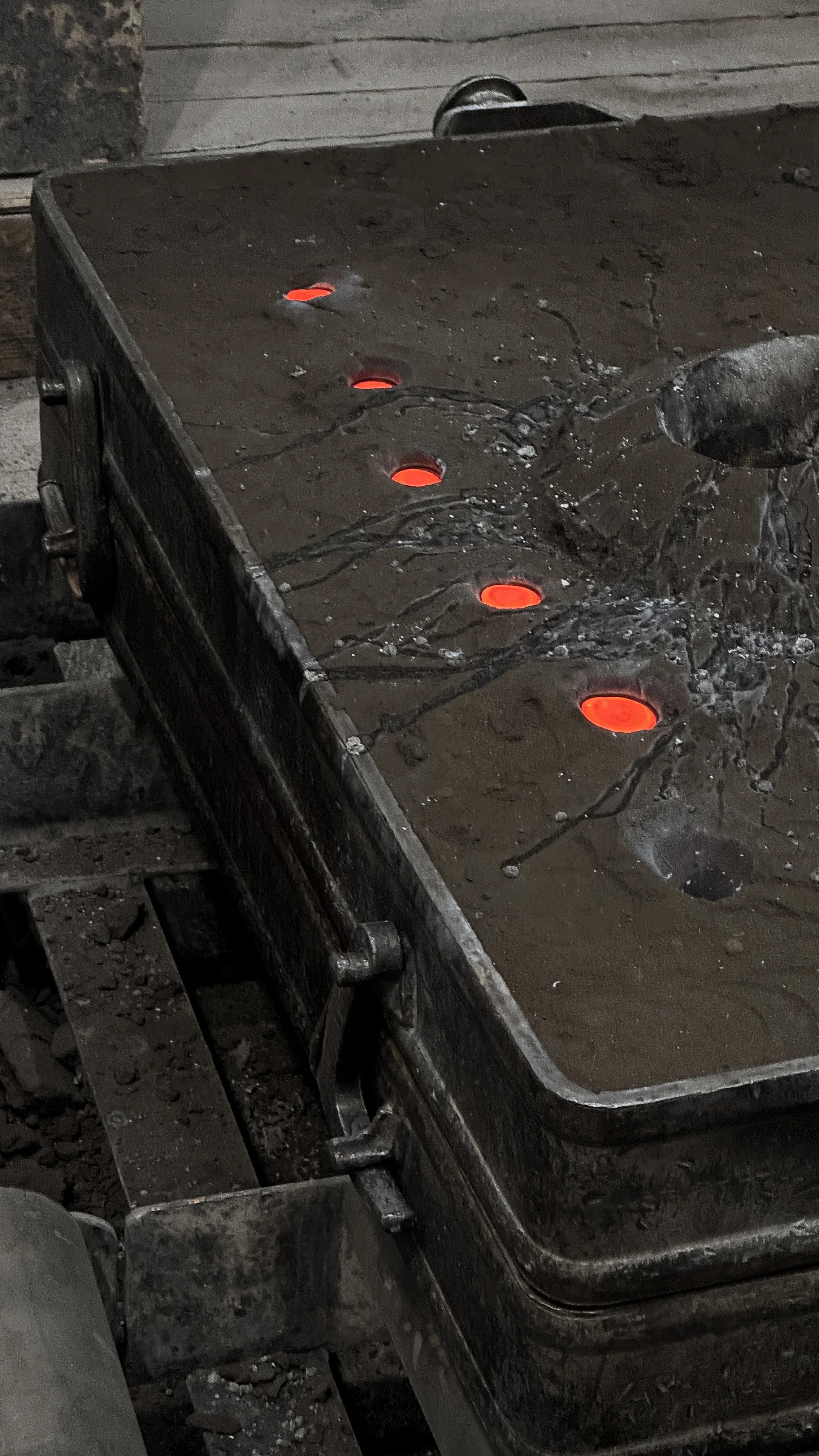 A steel worktable with glowing red-hot holes and a stream of water pouring onto it, indicating metal forging or welding process.