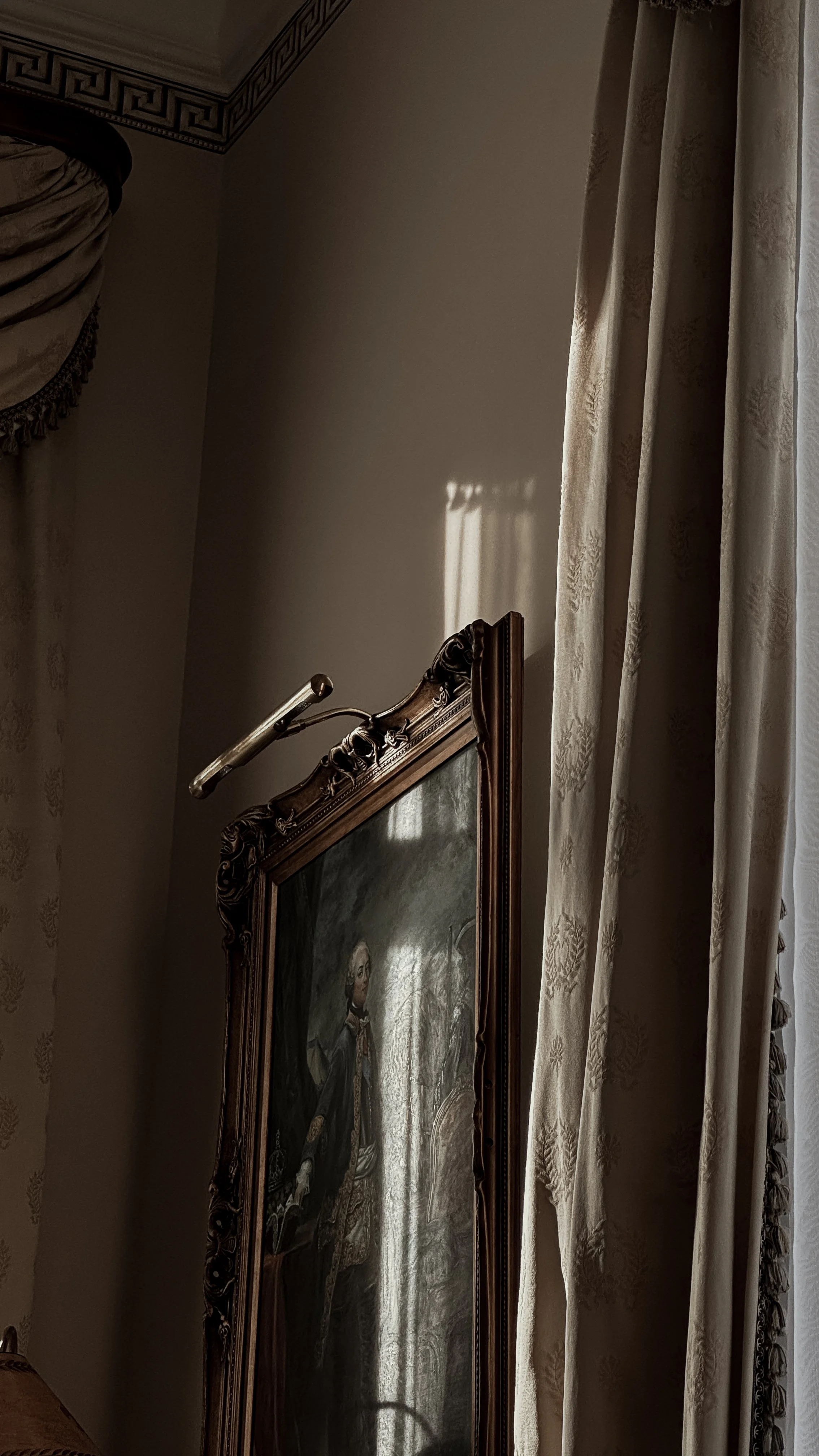 A vintage framed portrait of a regal man with a beard and mustache, wearing regal attire, in a softly lit room with ornate curtains.
