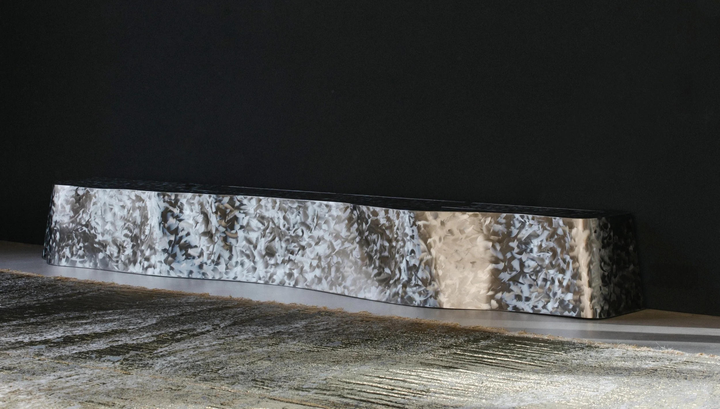 A modern, abstract sculpture with a textured, marbled surface in shades of white, gray, and black, placed on a flat surface against a dark background.