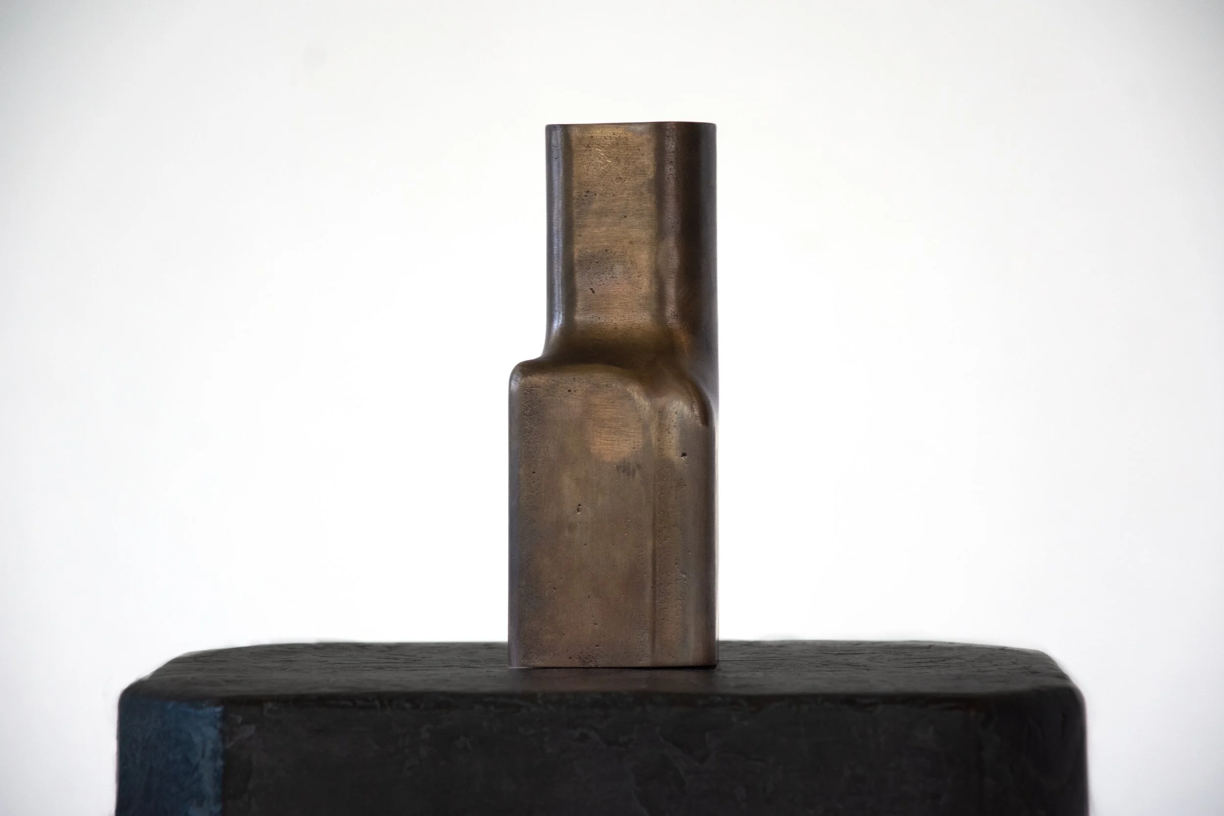 A bronze sculpture of an abstract, modern design on a black pedestal against a plain white background.