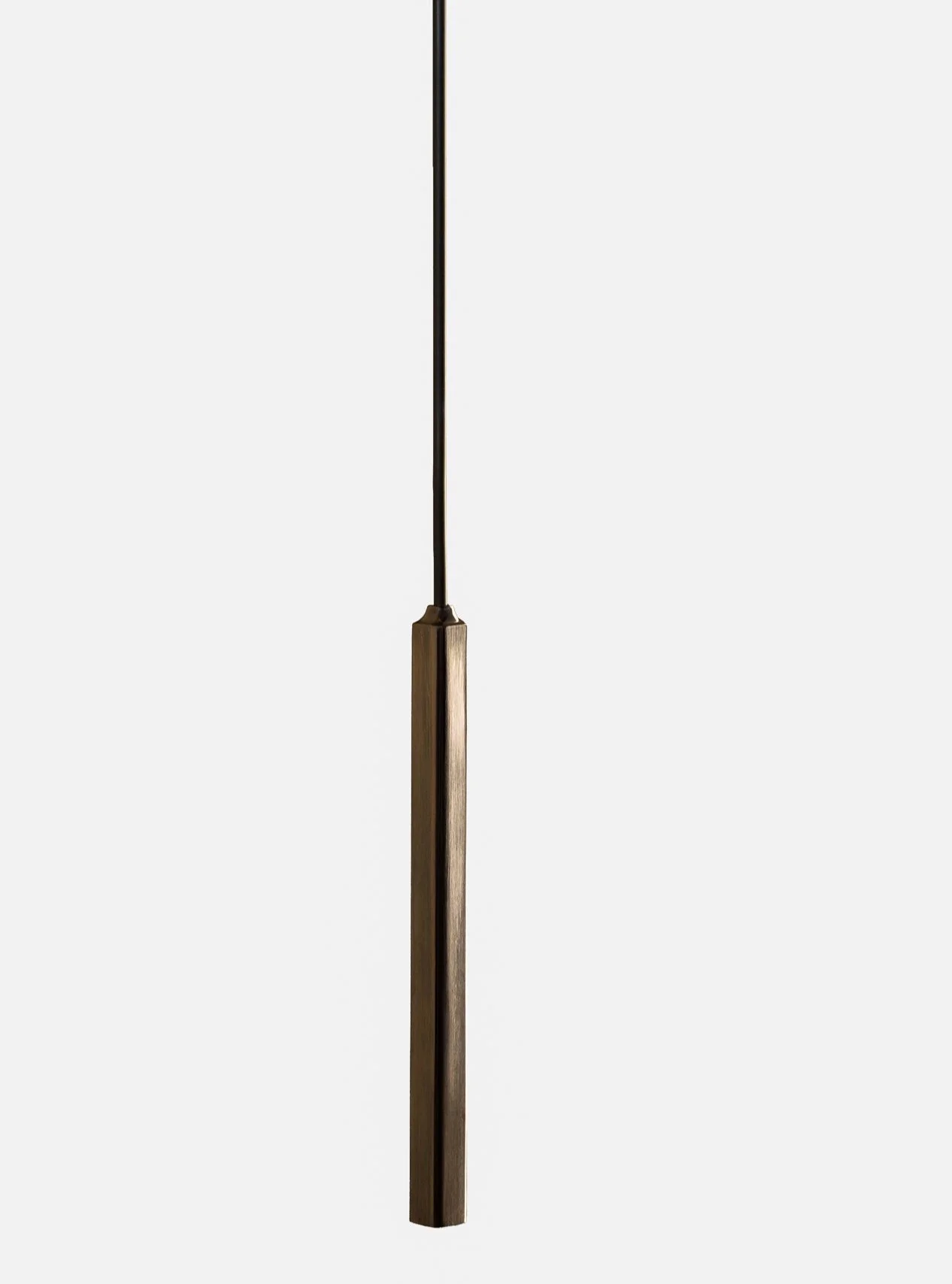 Close-up of a modern floor lamp with a vertical slender brass base and a thin black pole extending upward against a plain white wall.