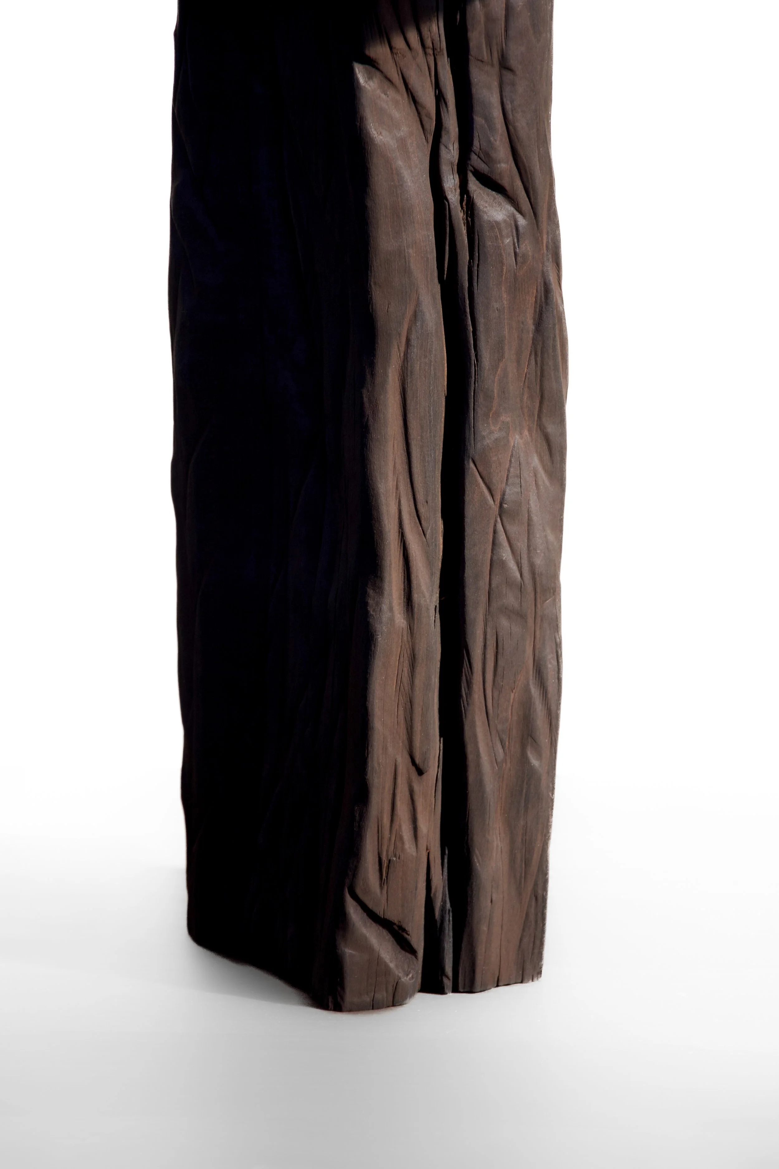 Close-up of a tall, irregularly shaped wooden sculpture with a natural, textured surface, standing on a white background.