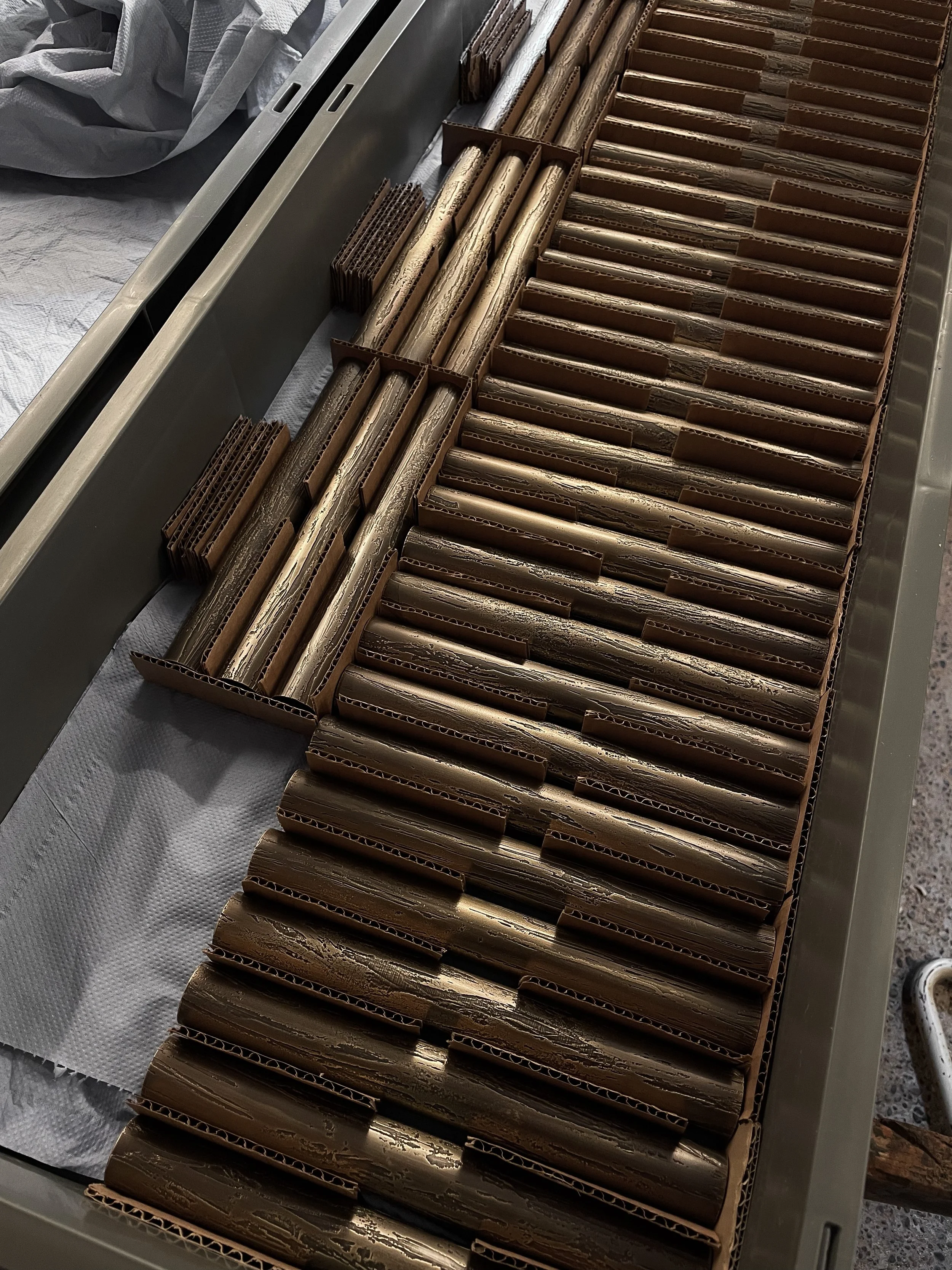 Rows of gold-colored metallic tubes or rods arranged neatly in cardboard trays on a metal table.