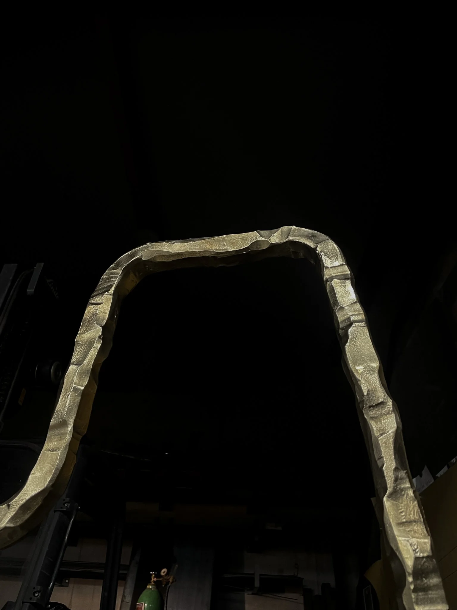 A large metallic structure with a curved shape, set against a dark background.