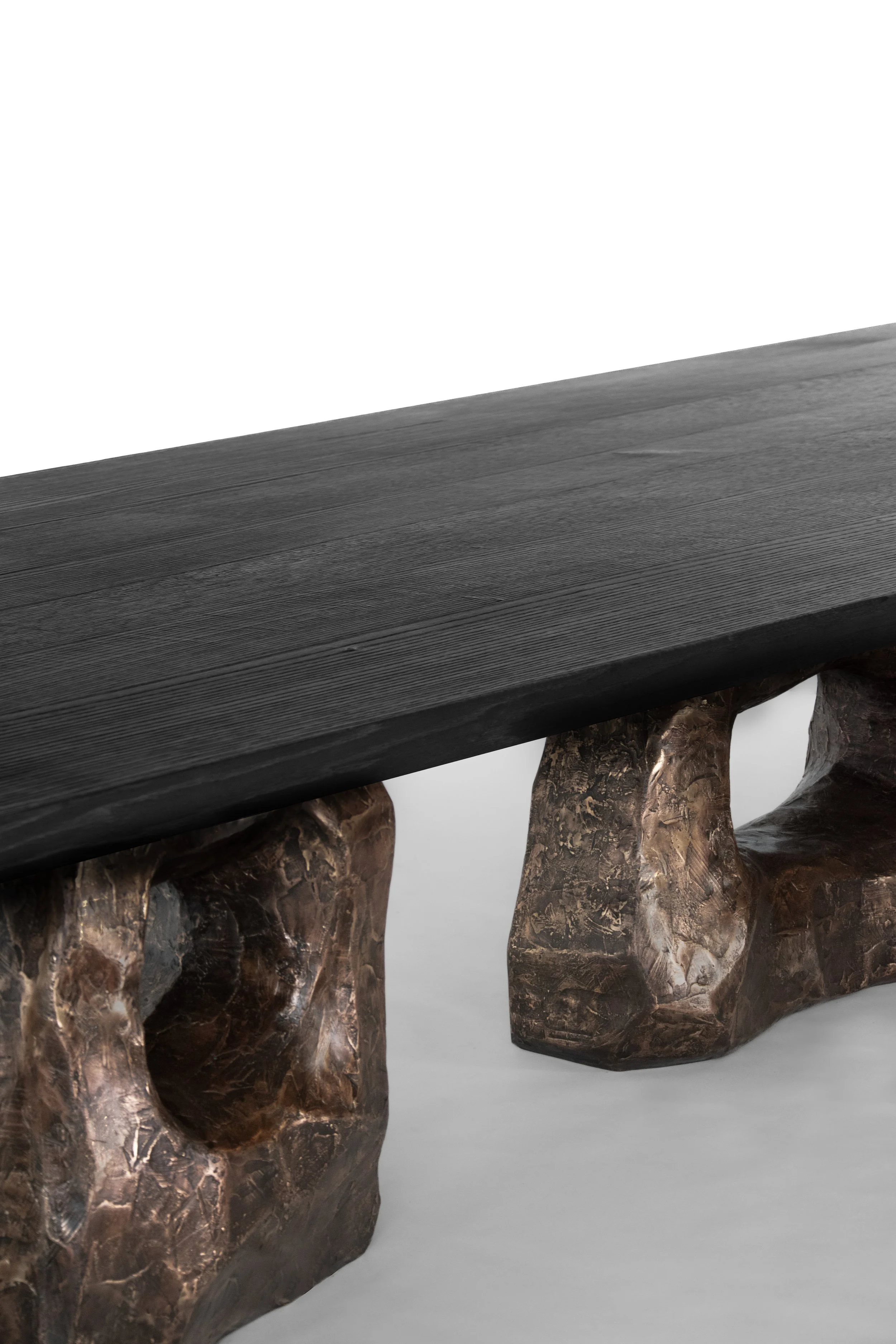 Close-up of a modern table with a black wooden top supported by irregular, textured bronze-colored metal legs.