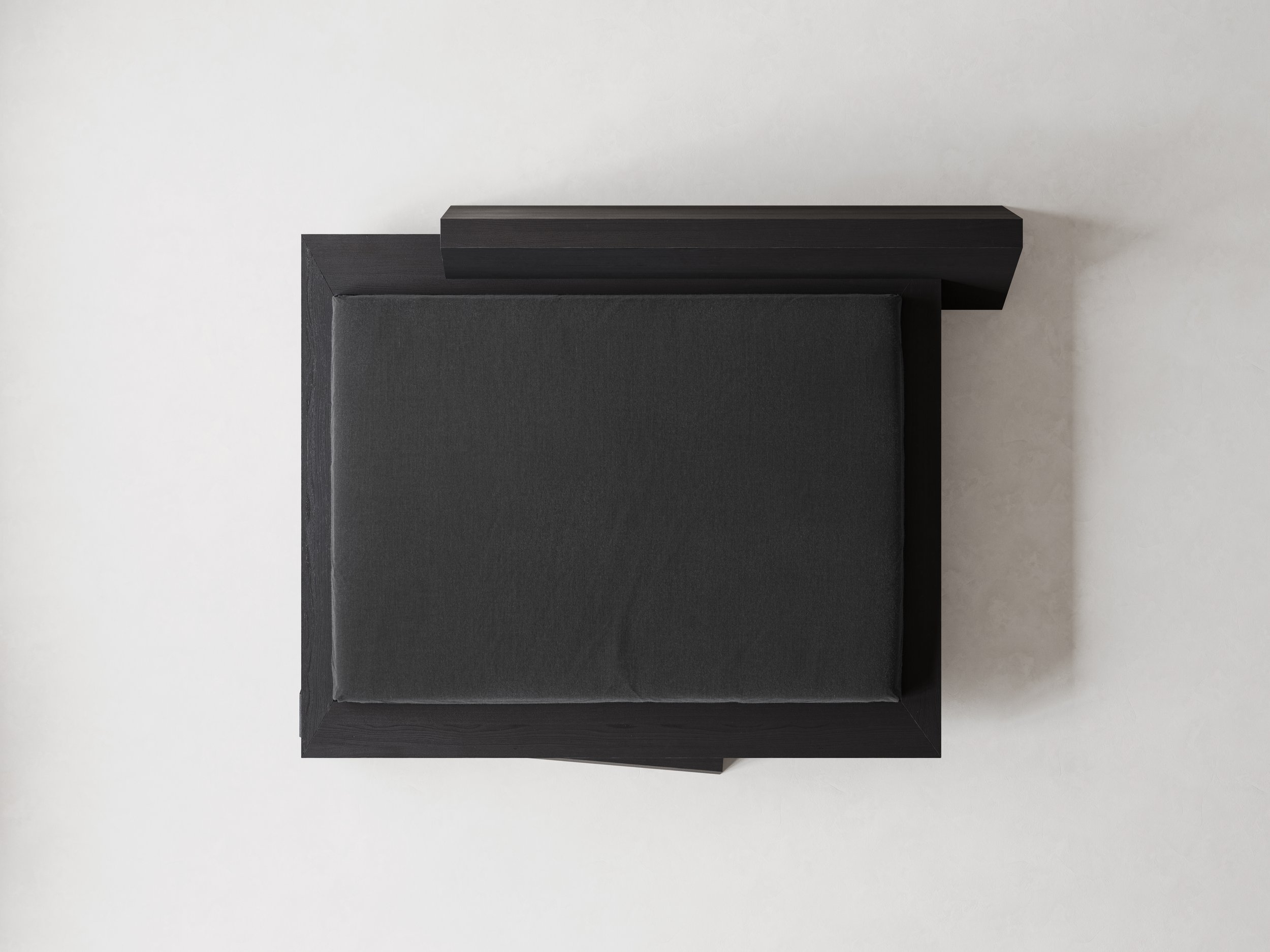 Top-down view of a modern black bed with a cushioned seat against a plain white wall.