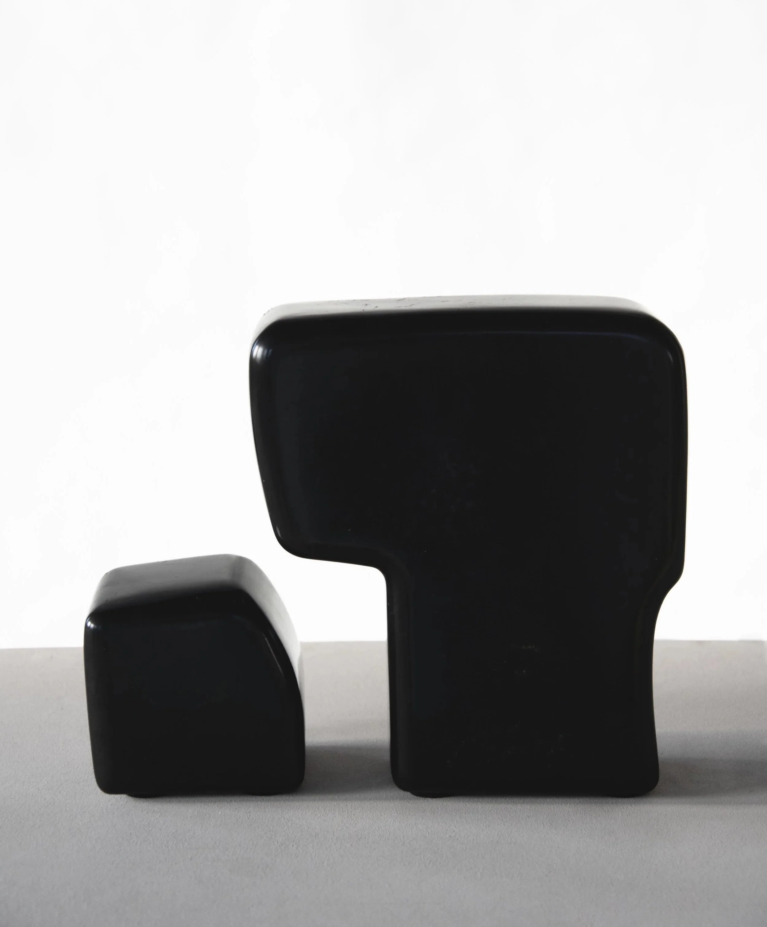 Black abstract sculptures with smooth, rounded shapes placed on a gray surface against a white background