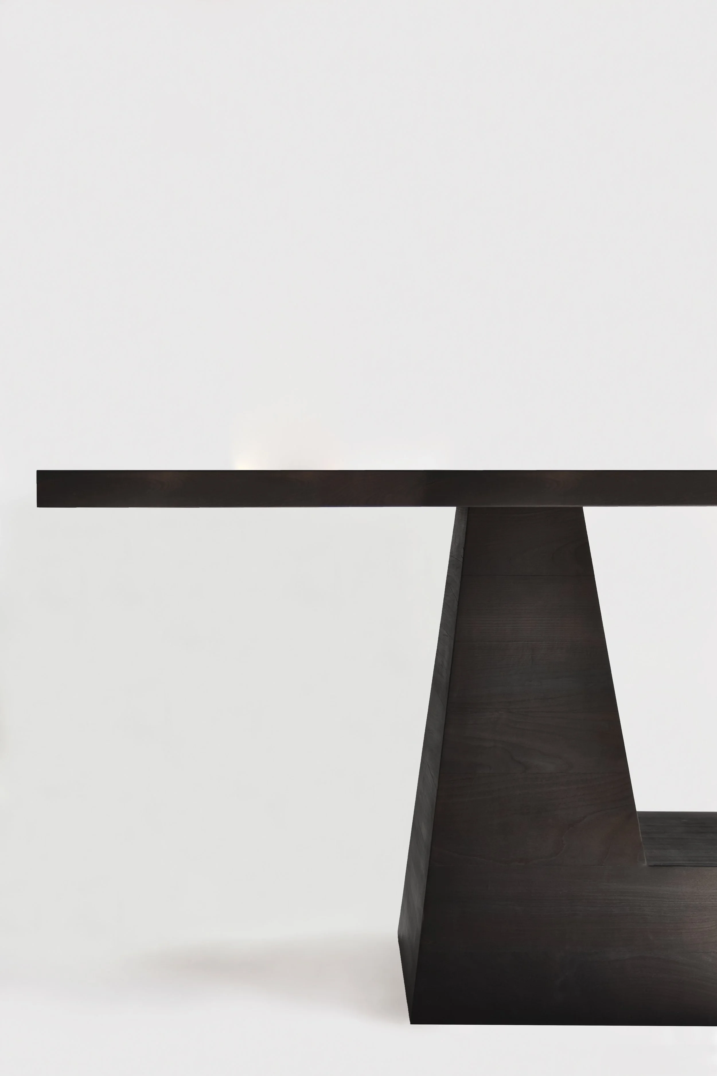 Close-up of a modern black wooden table with an angular geometric base, set against a plain white background.