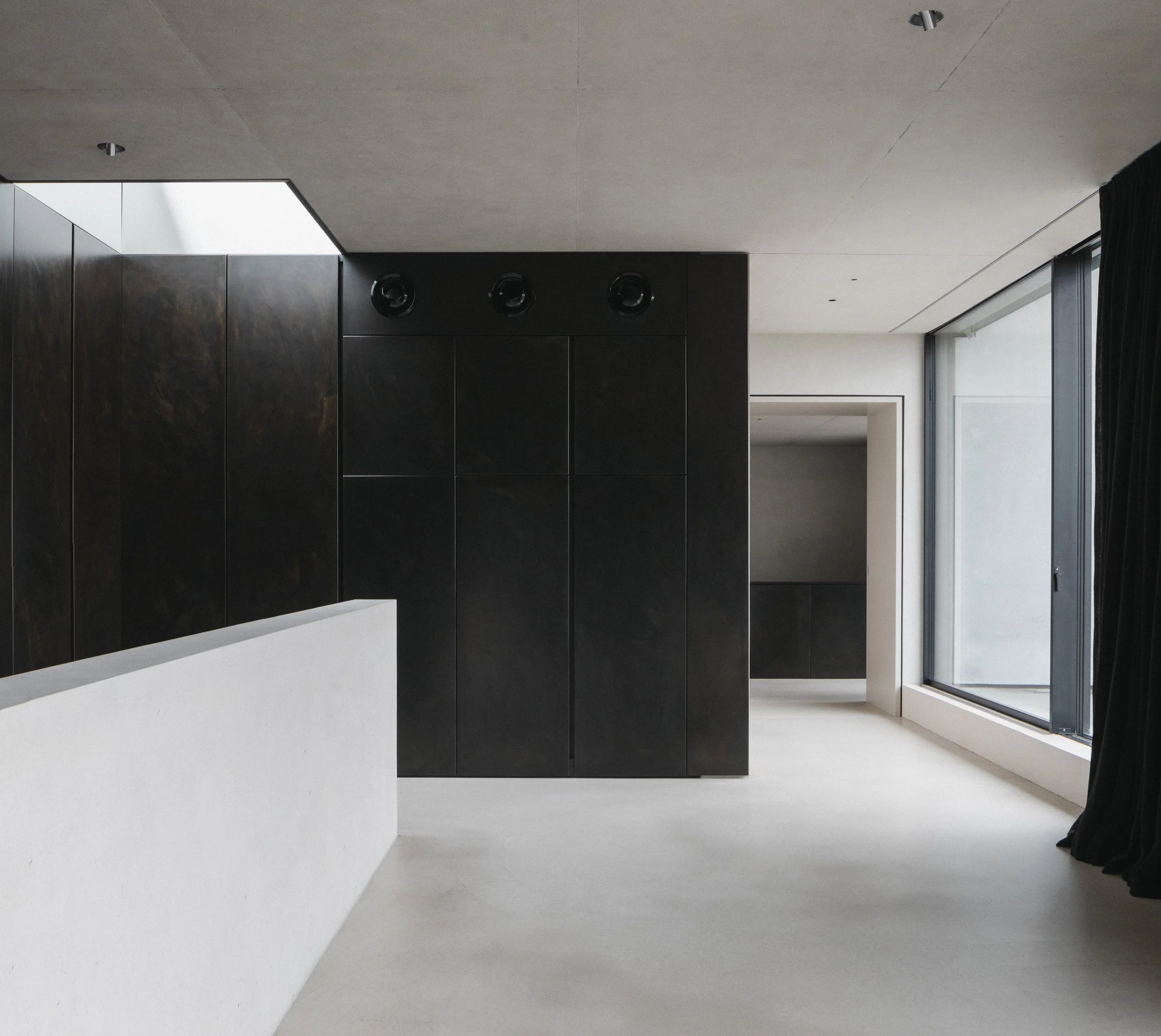 Modern interior space with black cabinets, large window with black curtains, white walls, and minimalist design.