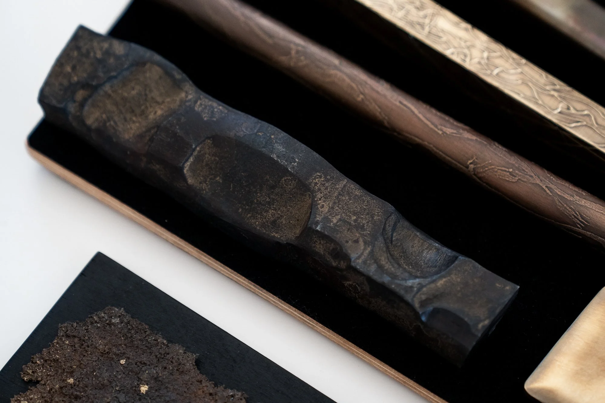 Ancient black stone sculpture with carved details, resting in a black display case, with a textured dark material on a separate black surface below.