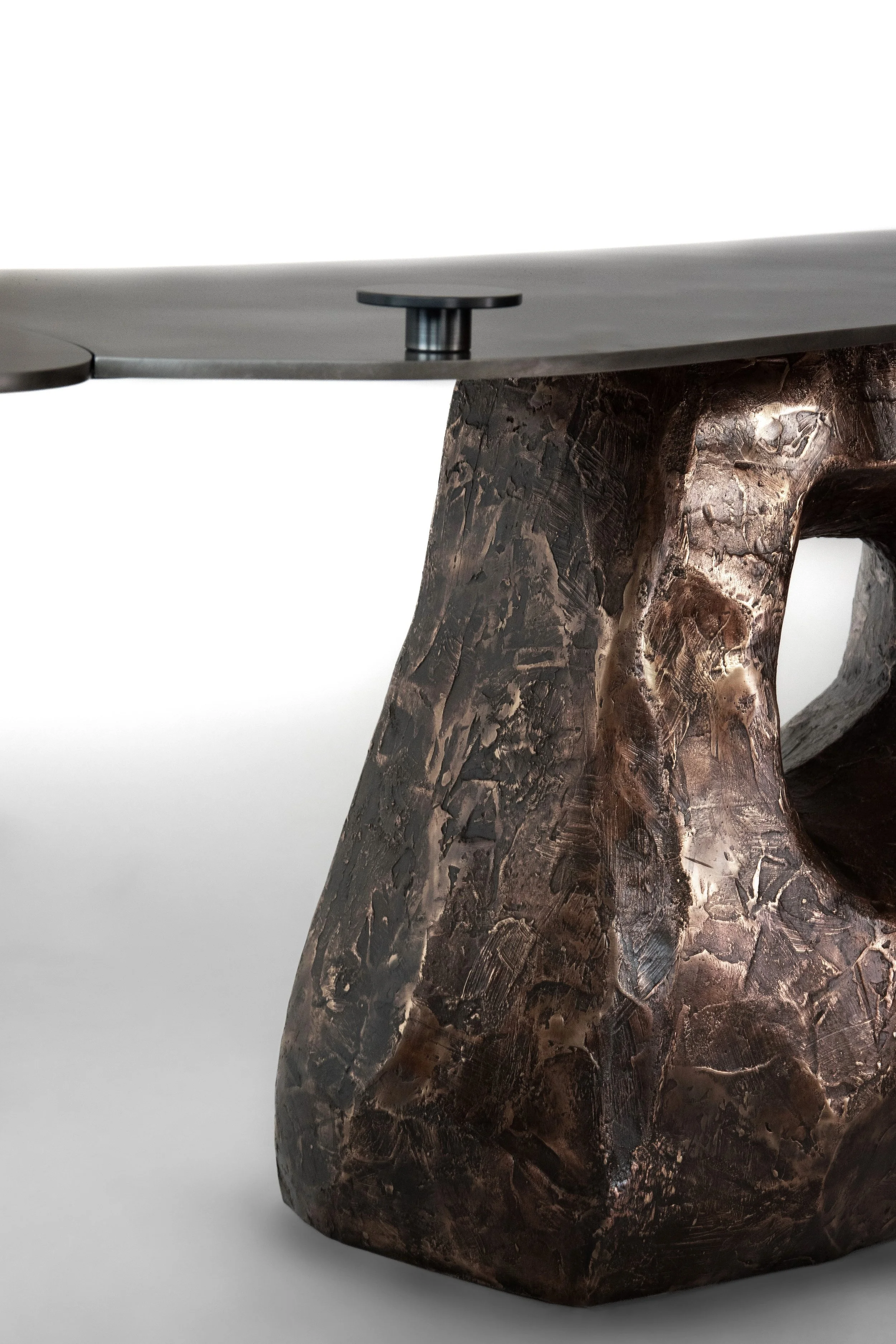 Close-up of a table with a thick, textured, dark bronze-colored base and a sleek metal top.