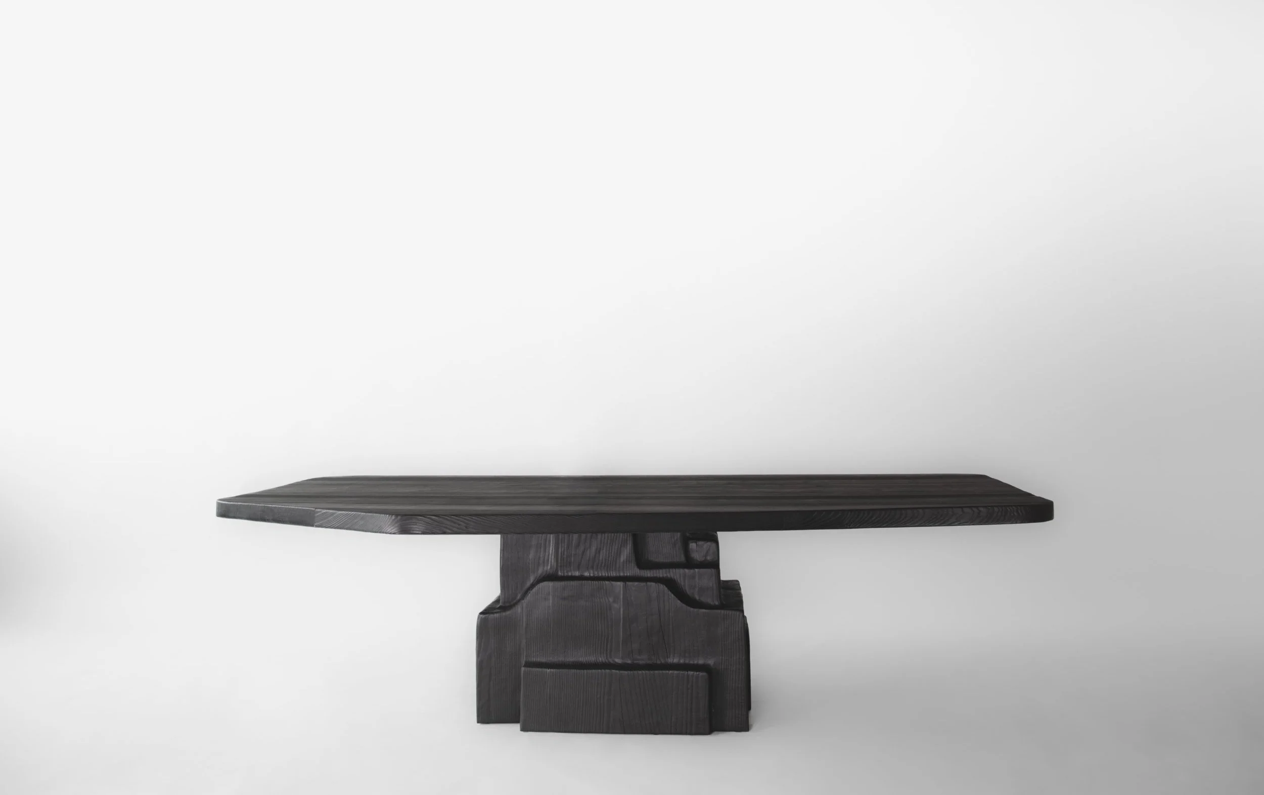 A dark wooden table with a thick, rectangular top and a sturdy, block-like base, set against a plain white background.