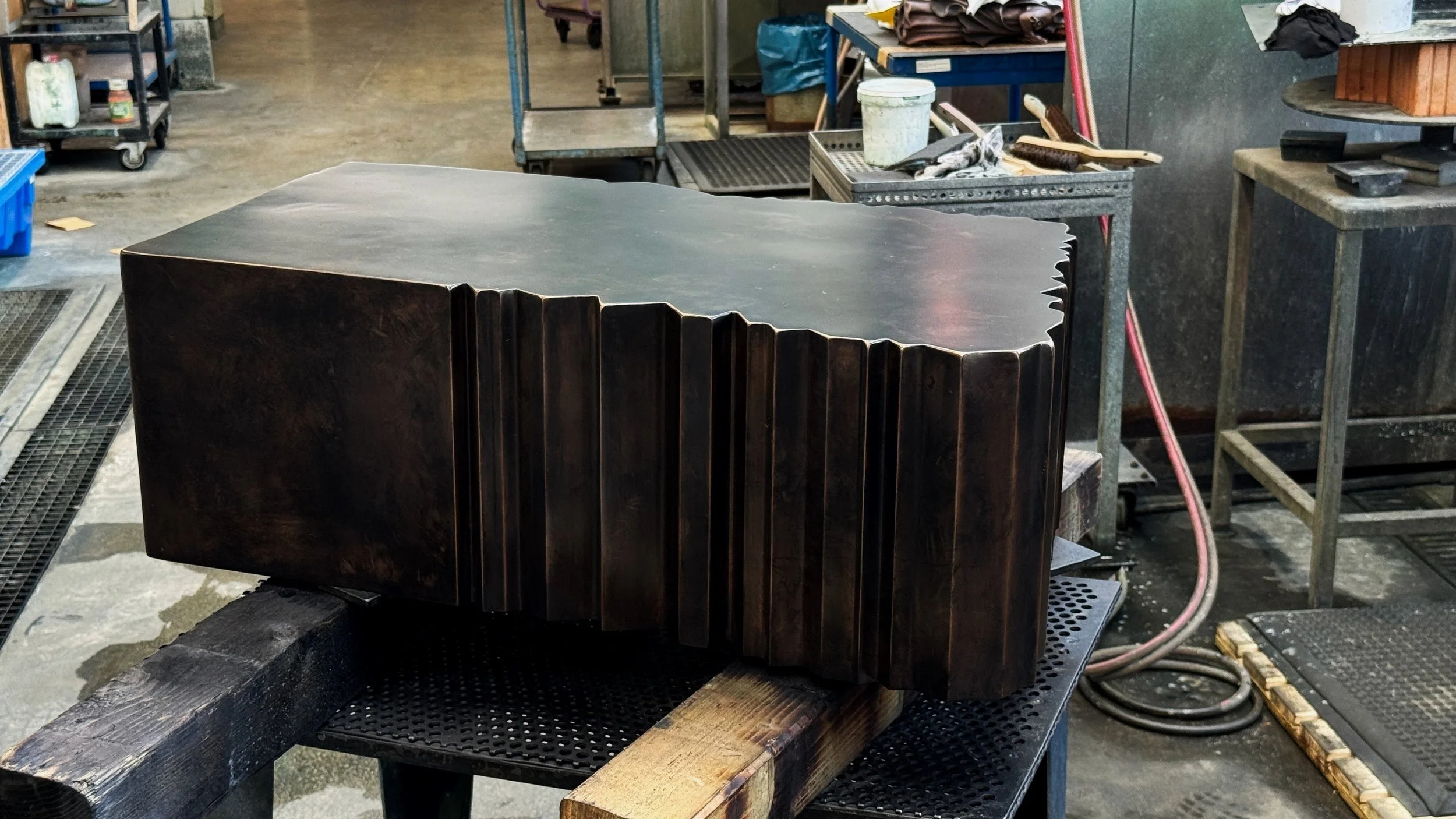 A large, dark wooden sculpture with carved vertical grooves, placed on a workbench in a workshop.