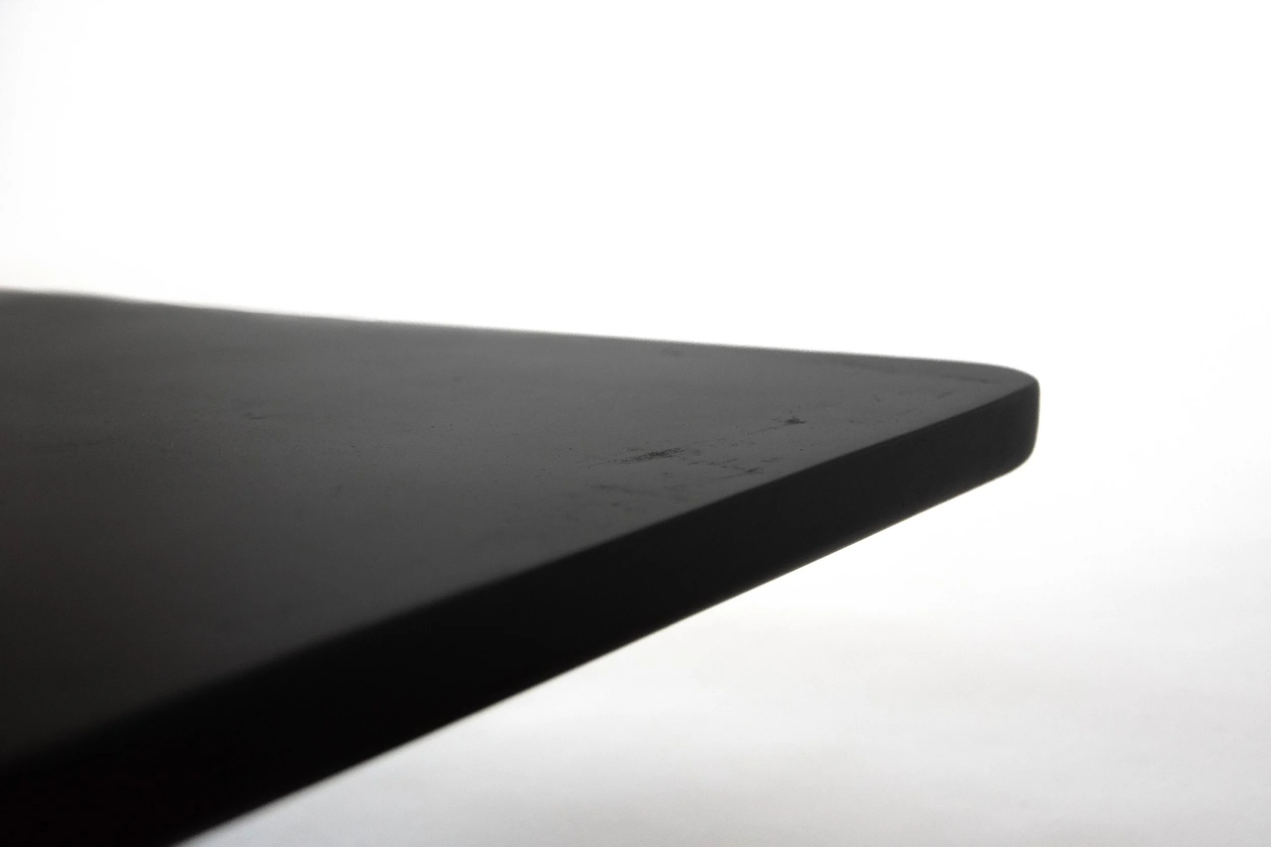 Close-up of the edge of a dark, smooth, possibly black, rectangular object against a bright white background.