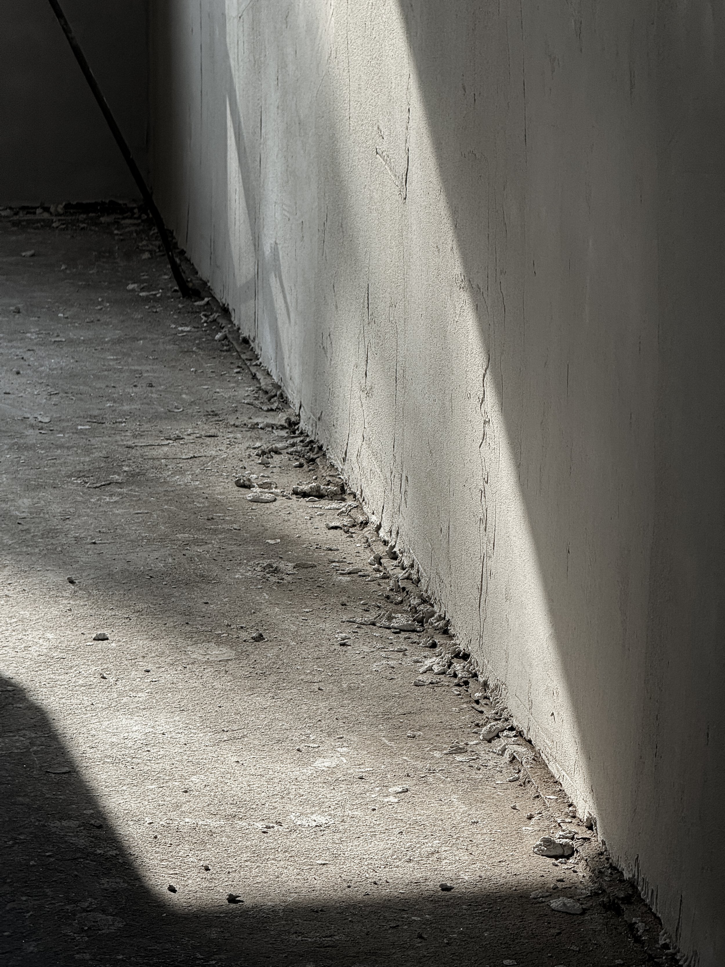 Concrete pathway beside a painted wall with cracks, debris, and a shadow cast over part of the ground.