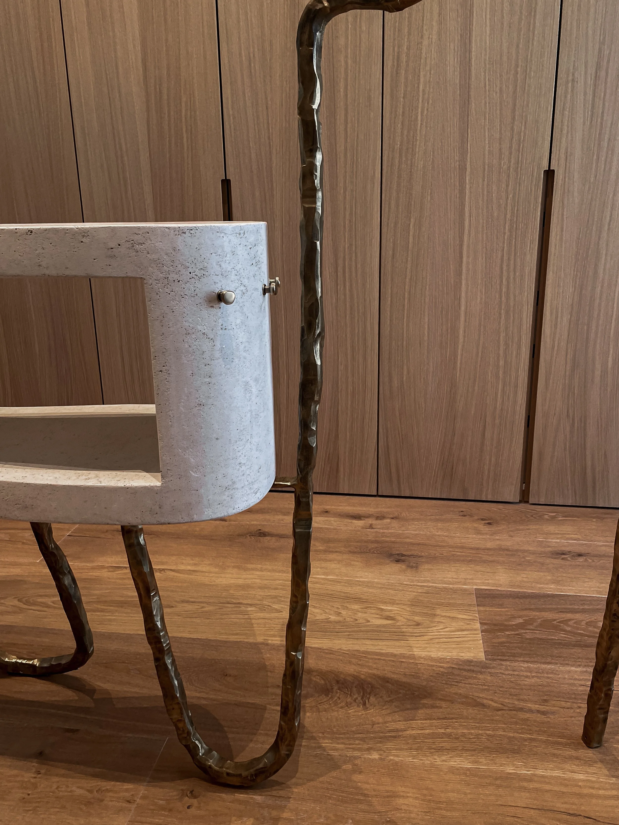 Part of a modern chair with a circular concrete seat and curved metal legs, against a wooden cabinet background.