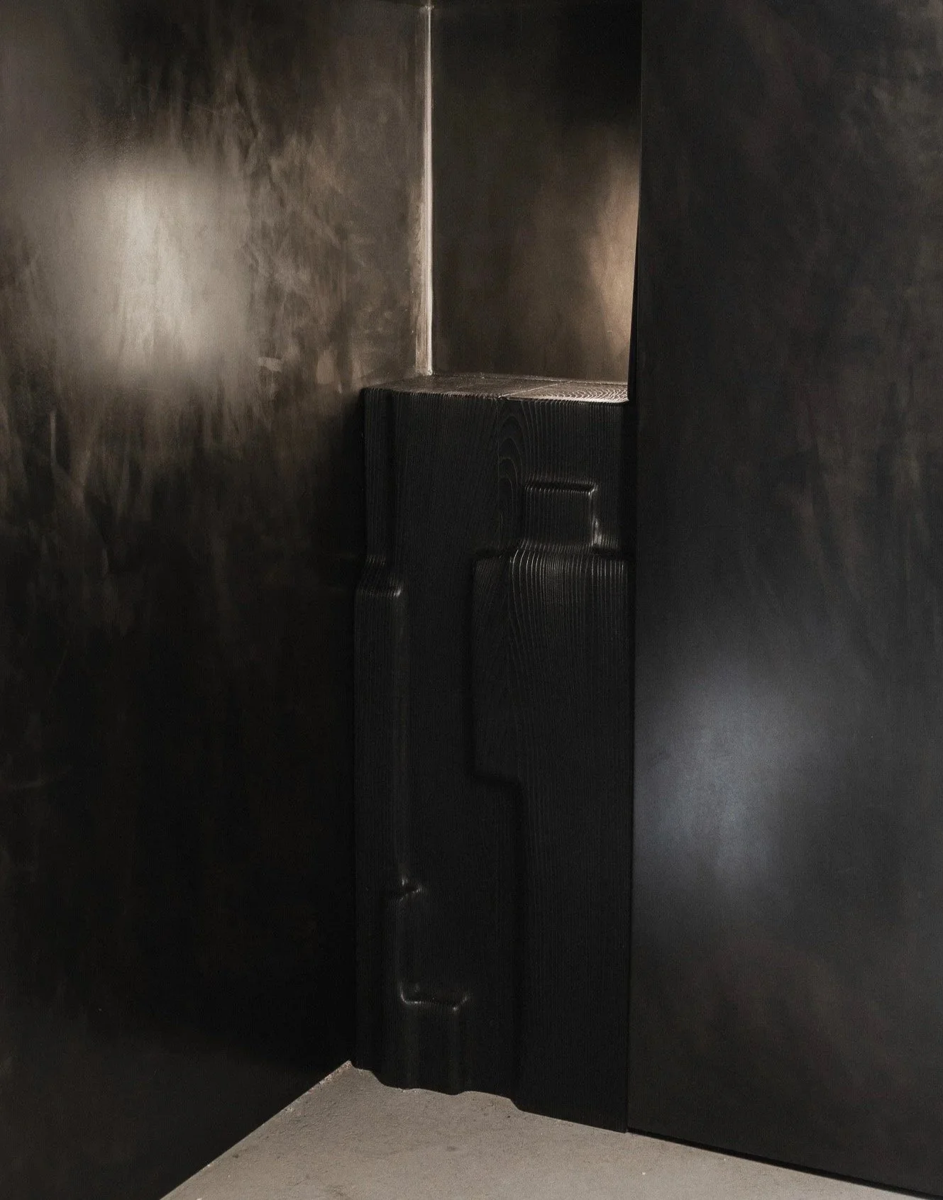 Close-up of black shelving or furniture piece with a textured surface in a dark room.