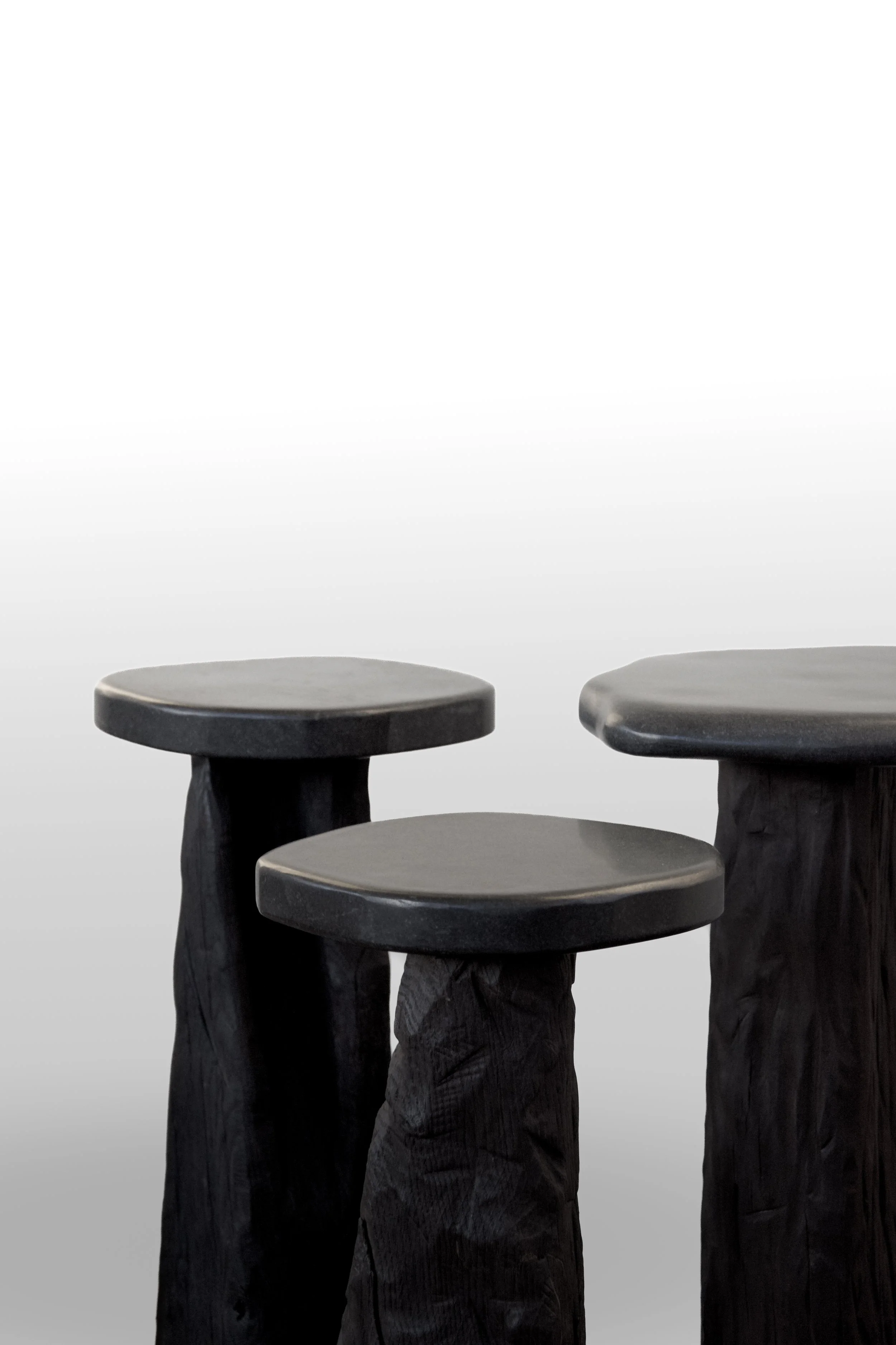 Three dark wooden stools with round seats against a gradient background.