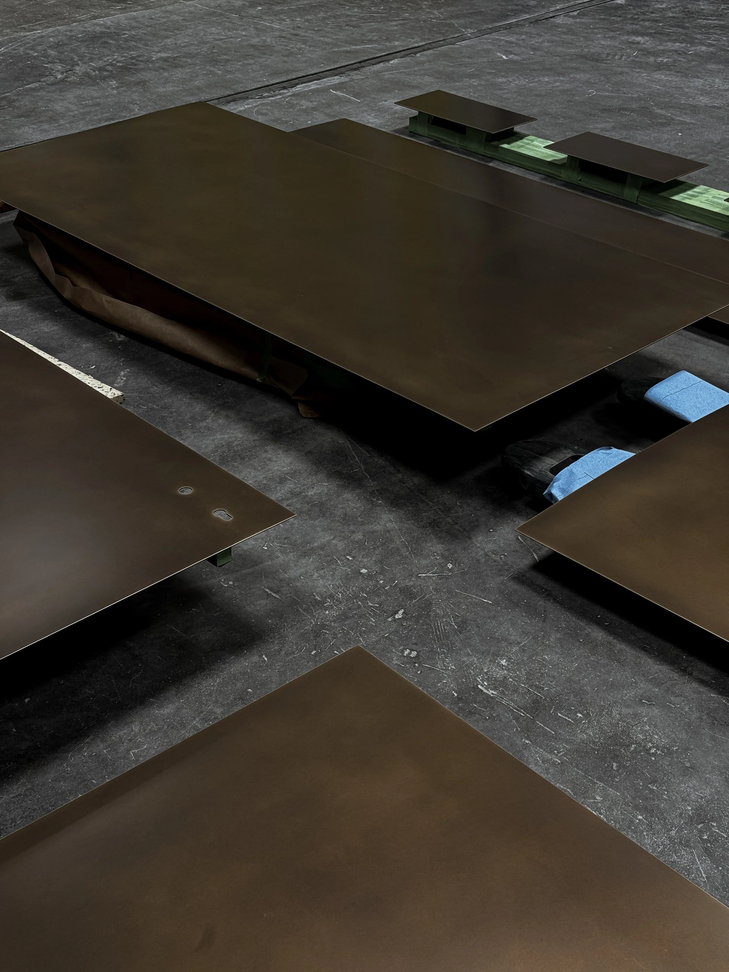 Three metal sheets, possibly car hoods or large panels, resting on a dark, concrete floor.