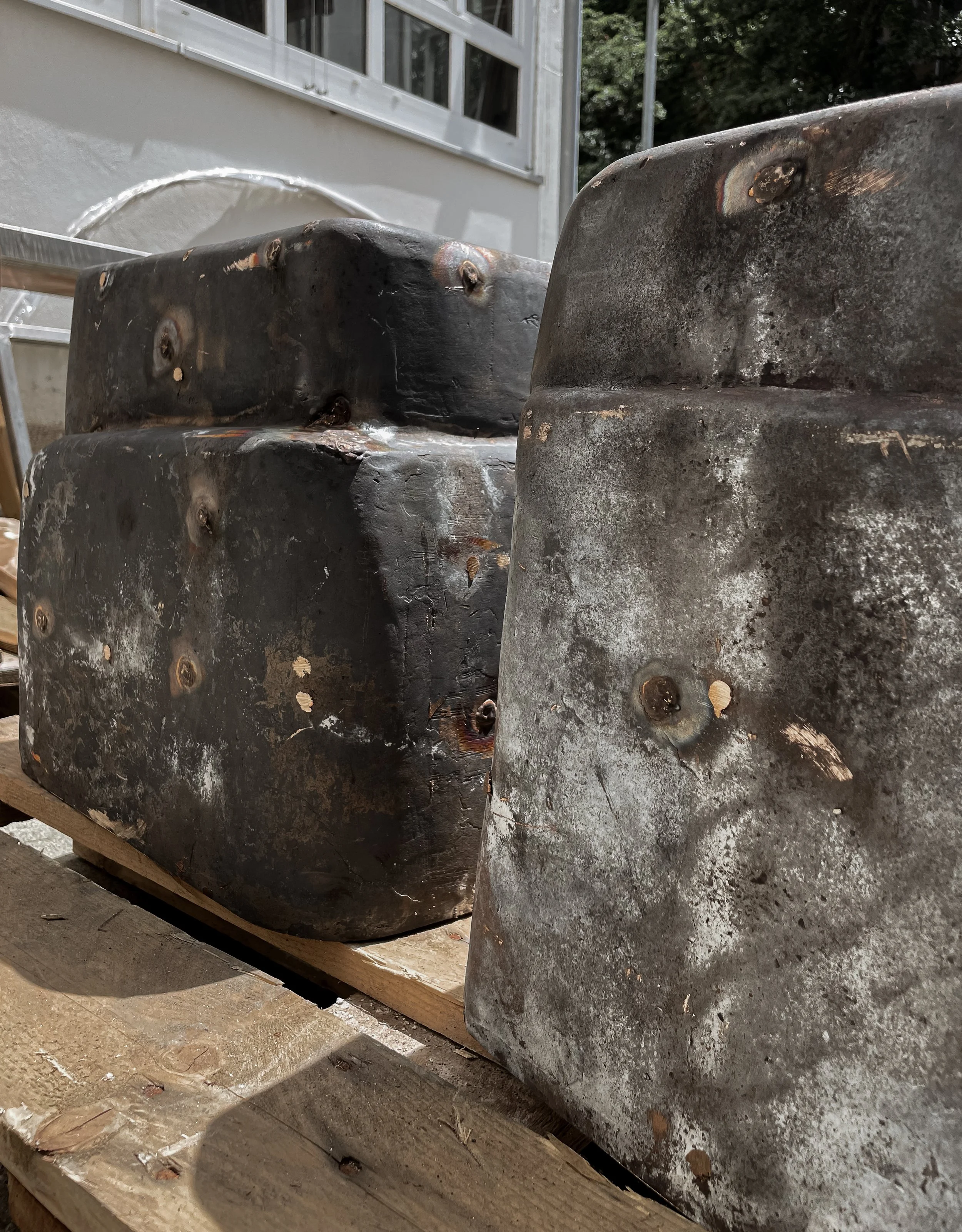 Stack of weathered metal molds or blocks with rust and scratches on a wooden pallet outdoors.