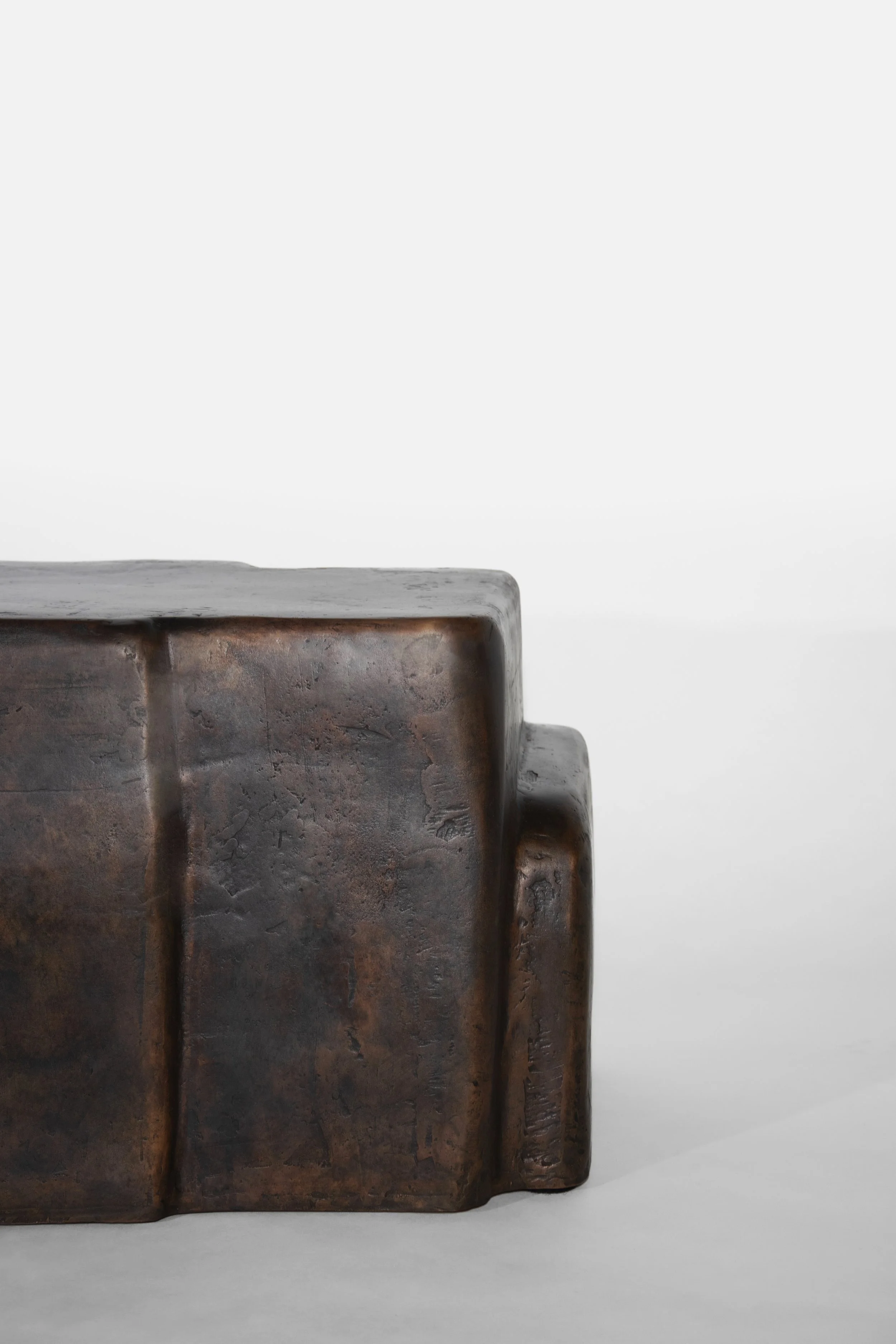Close-up of a rustic, rectangular, metallic sculpture with a textured, weathered surface in bronze and copper tones, set against a plain white background.