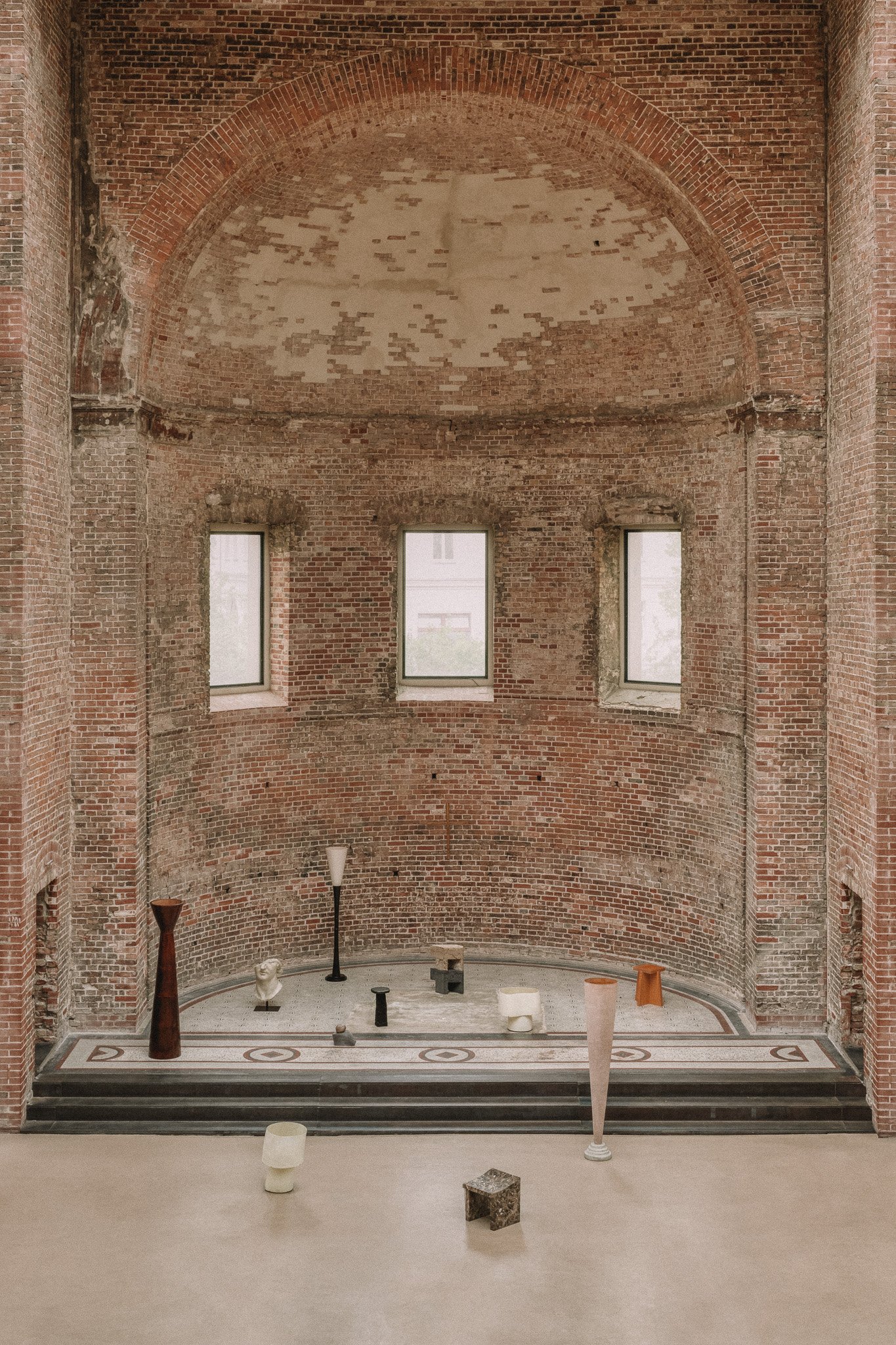 Brick interior with three rectangular windows, a brick arch ceiling, and various modern sculptures on a stage.