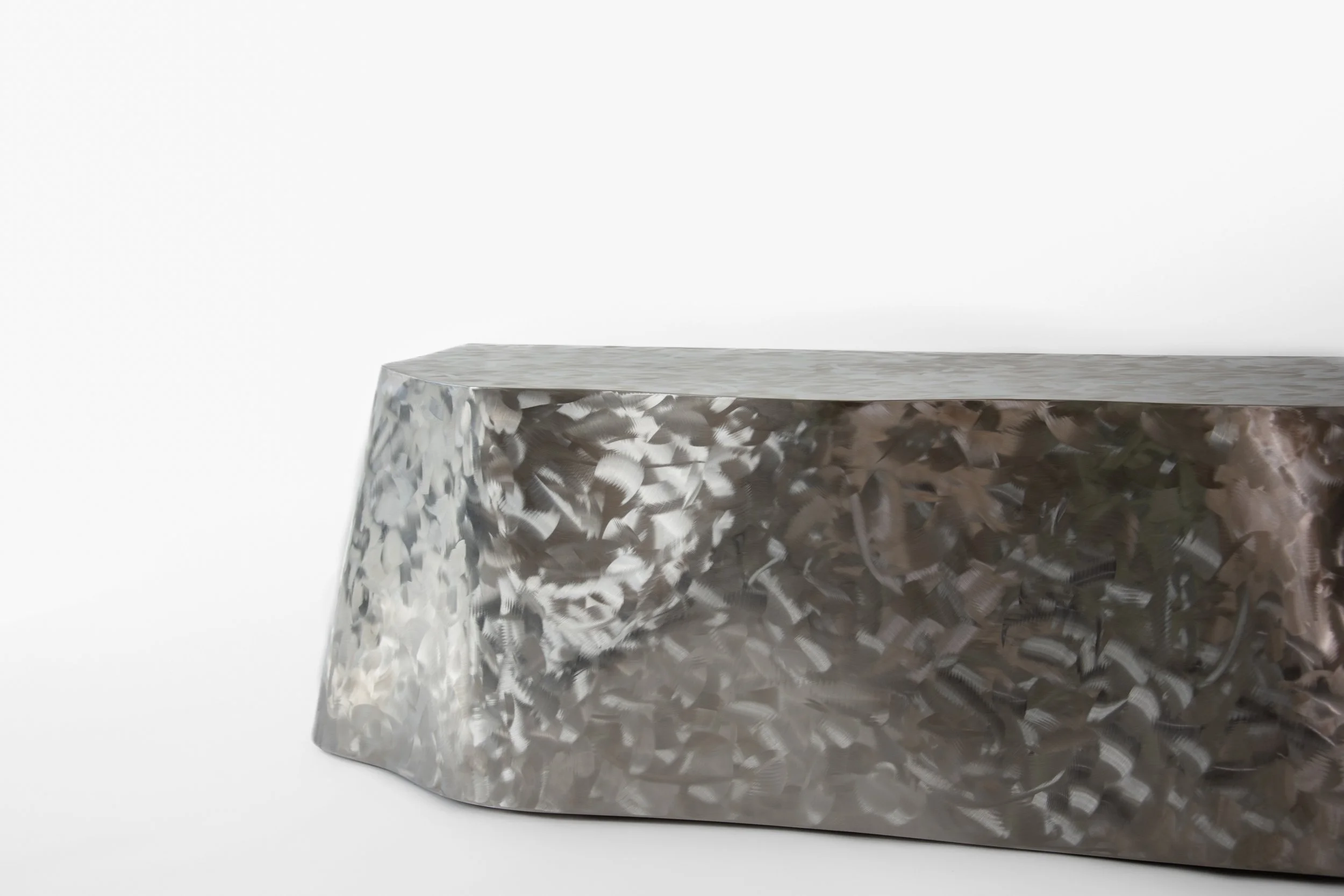 A metallic, textured cylindrical object with a reflective surface featuring a pattern of irregular shapes, placed on a white background.