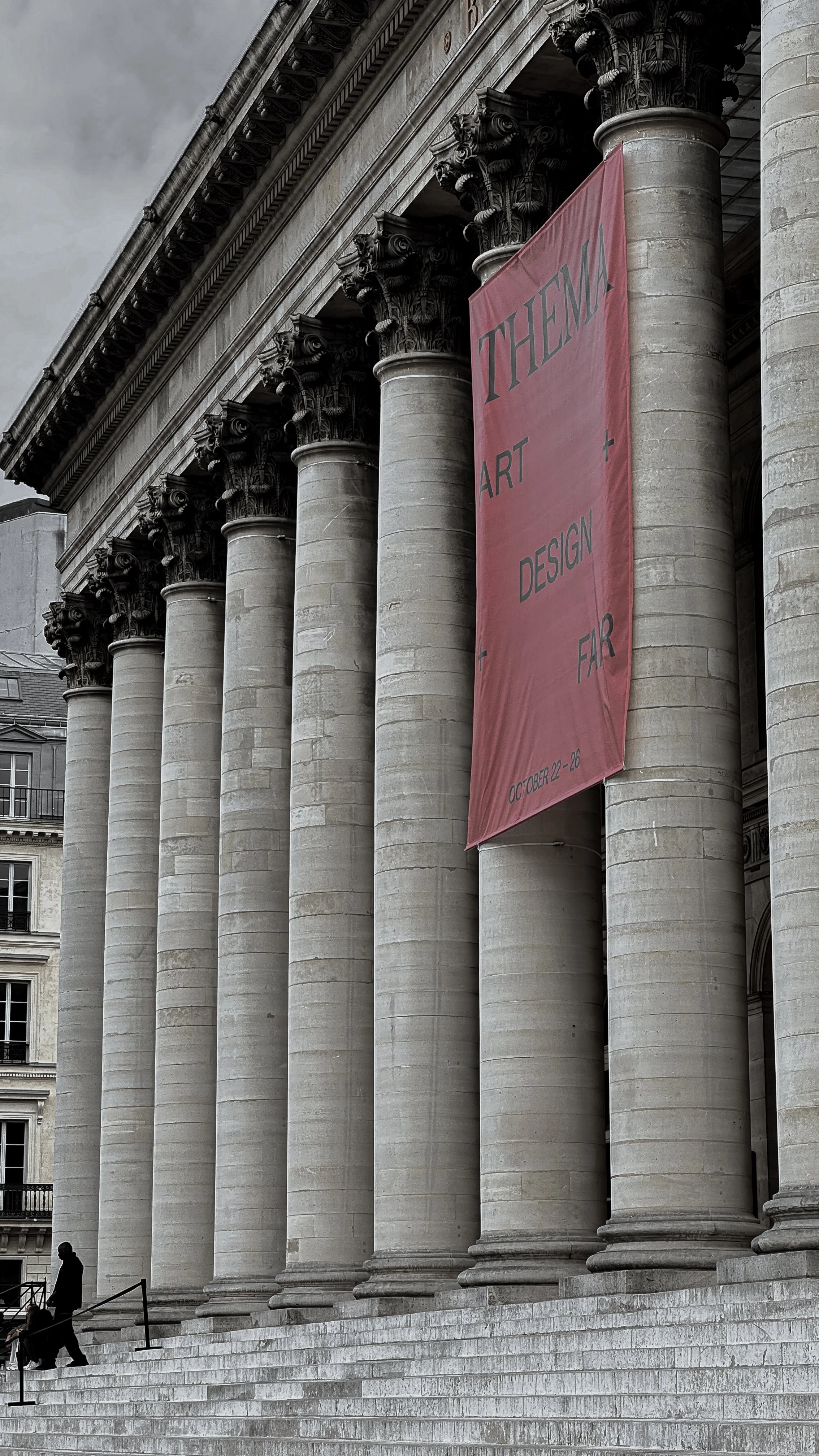 The image shows the front facade of a grand, historic building with large stone columns. A pink banner hanging between two columns reads, 'THEA ART + DESIGN FAIR' and includes the dates October 22-26.