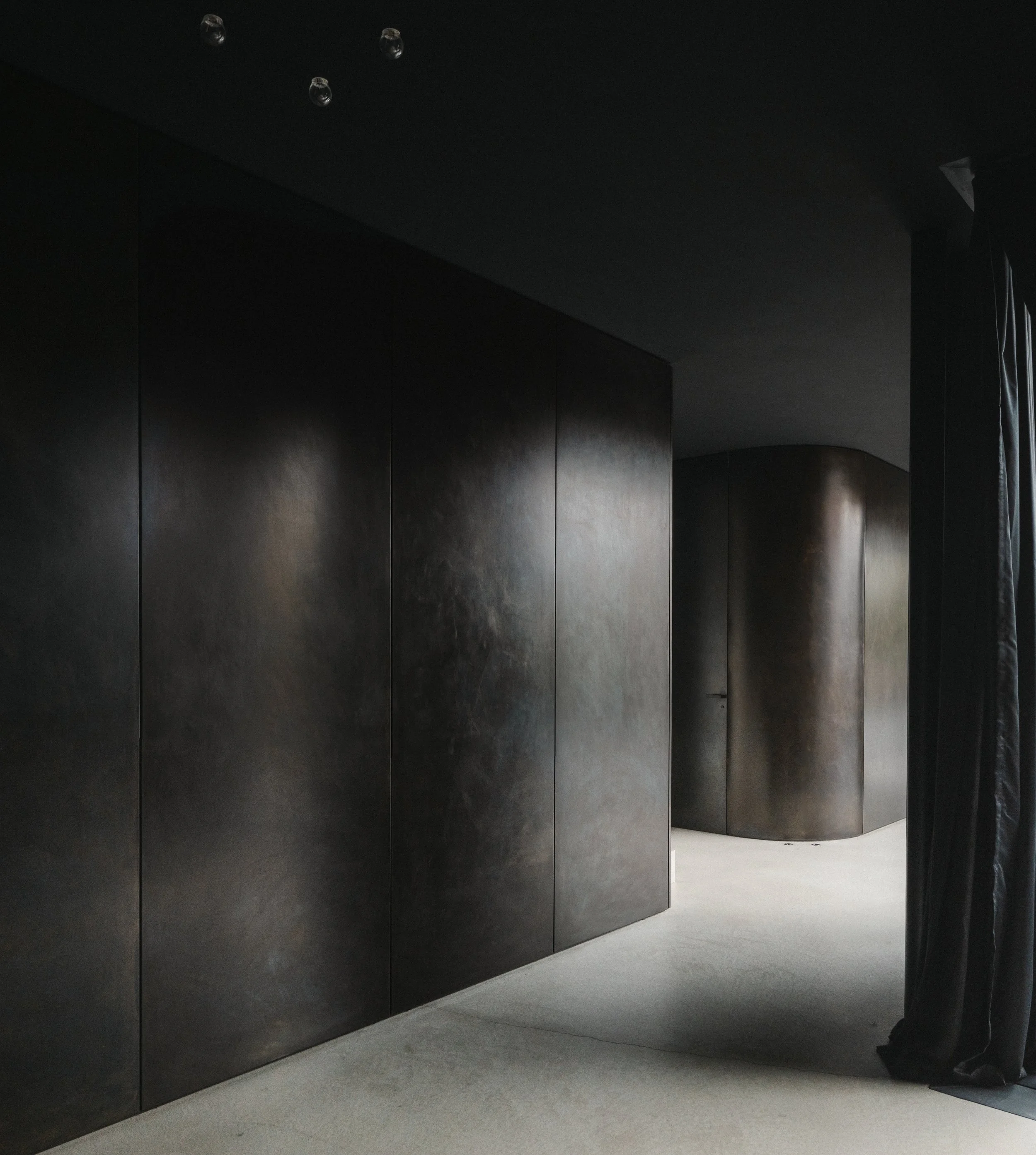 Dark, curved walls in a modern interior space with black curtains partially visible on the right.