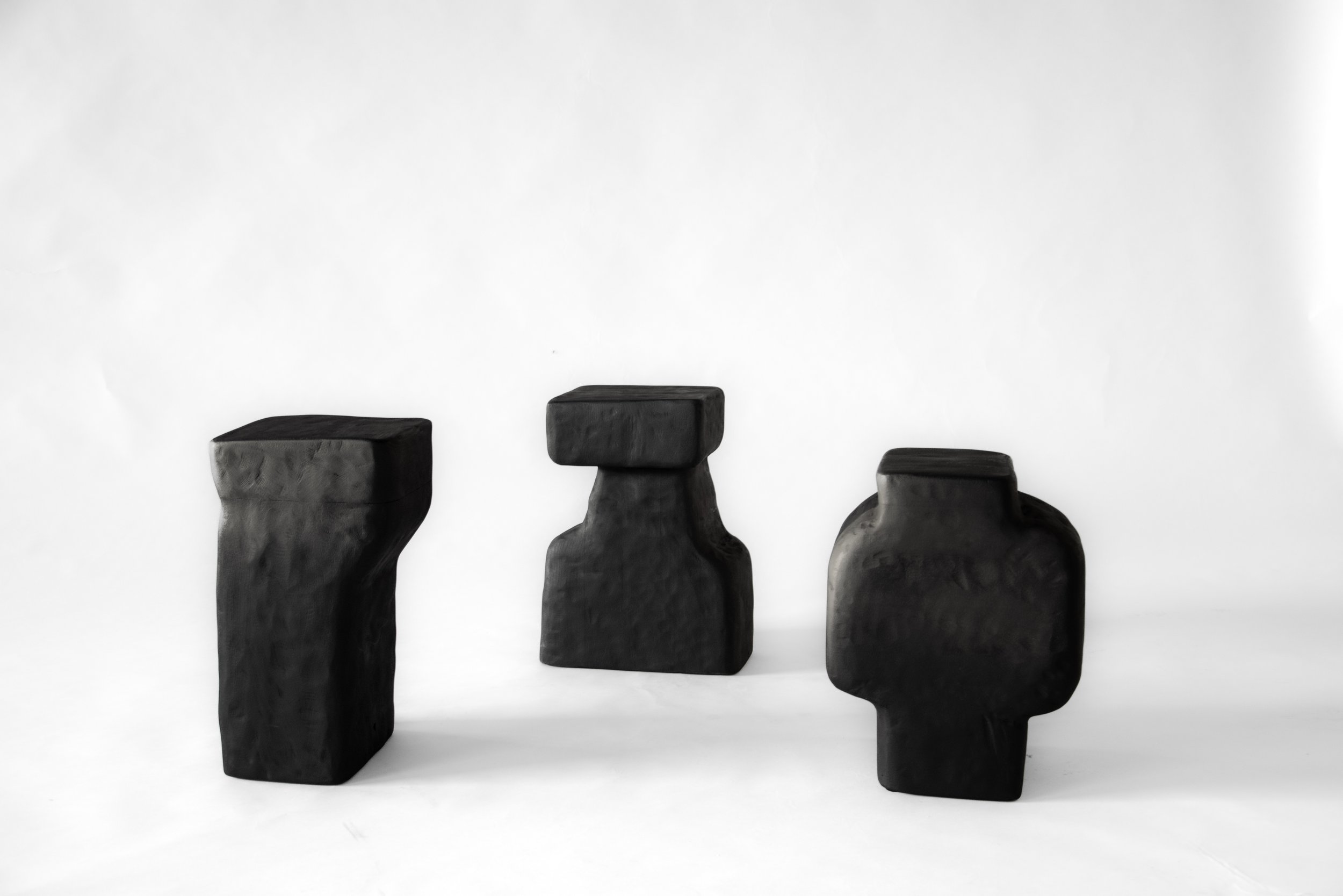 Three black abstract sculptures with irregular shapes and smooth textures, placed on a white background.