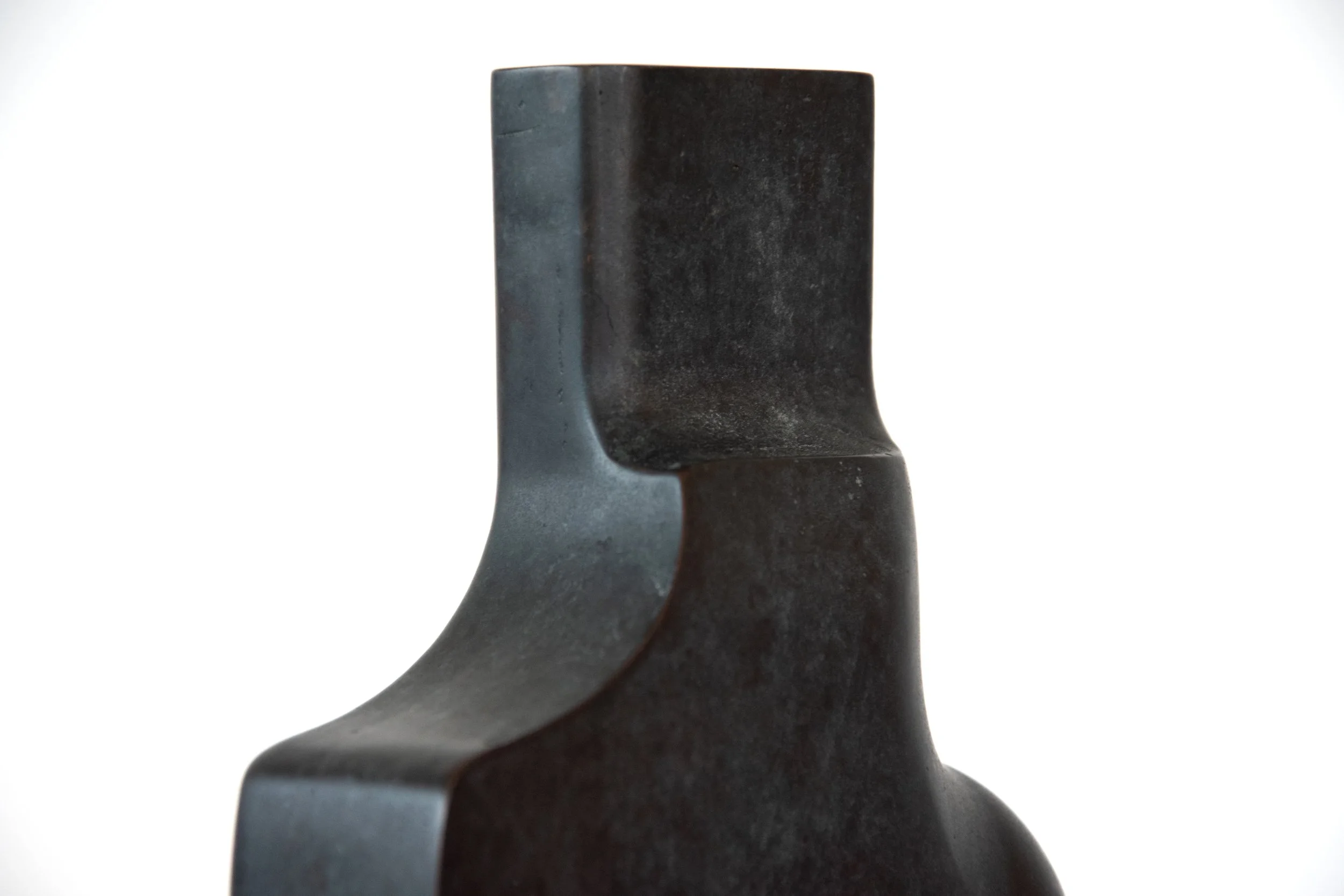 Close-up of a dark, textured sculpture with an abstract, curved form against a plain white background.