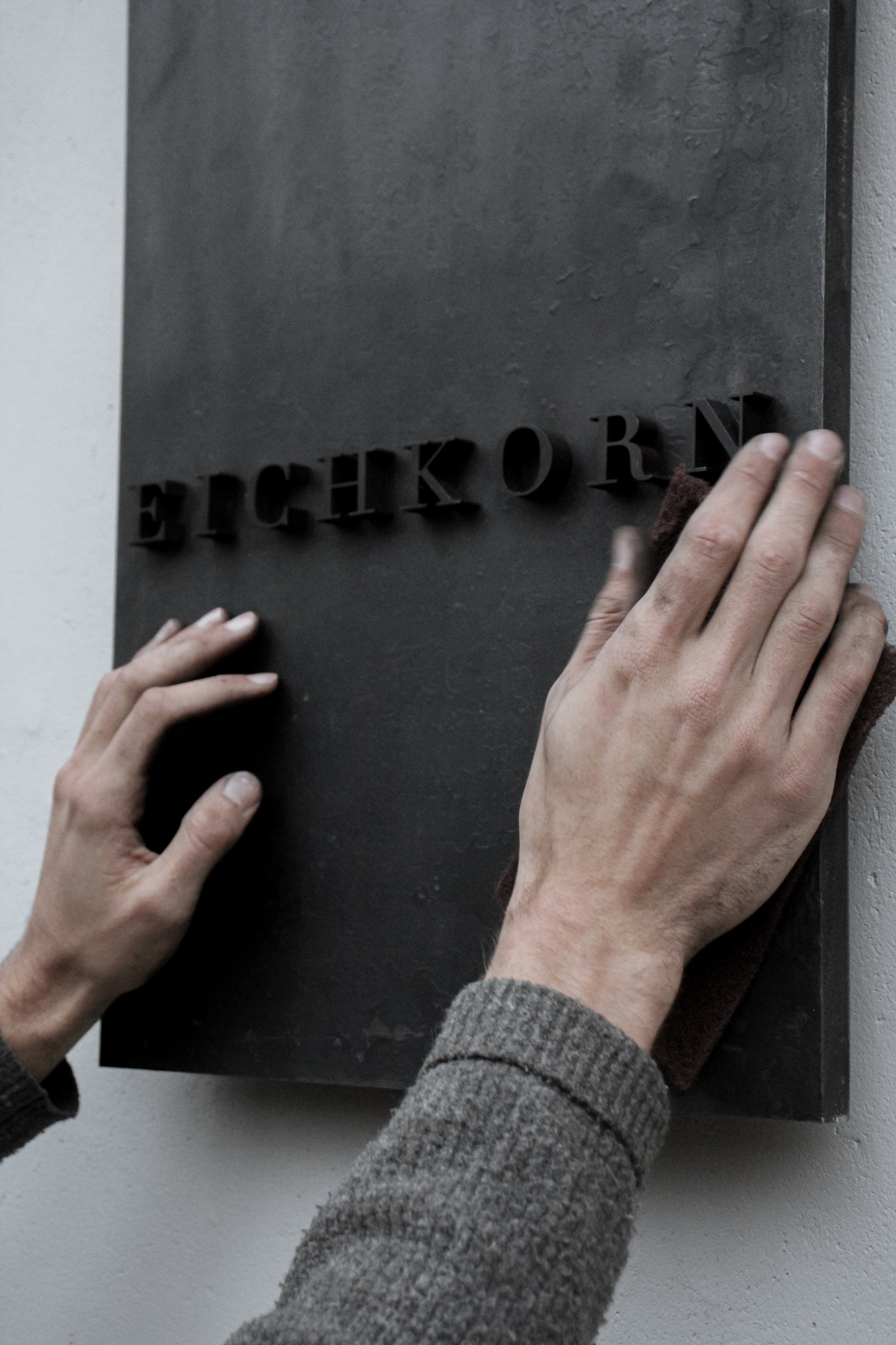 Person cleaning a black metal sign with cut-out letters on a wall.