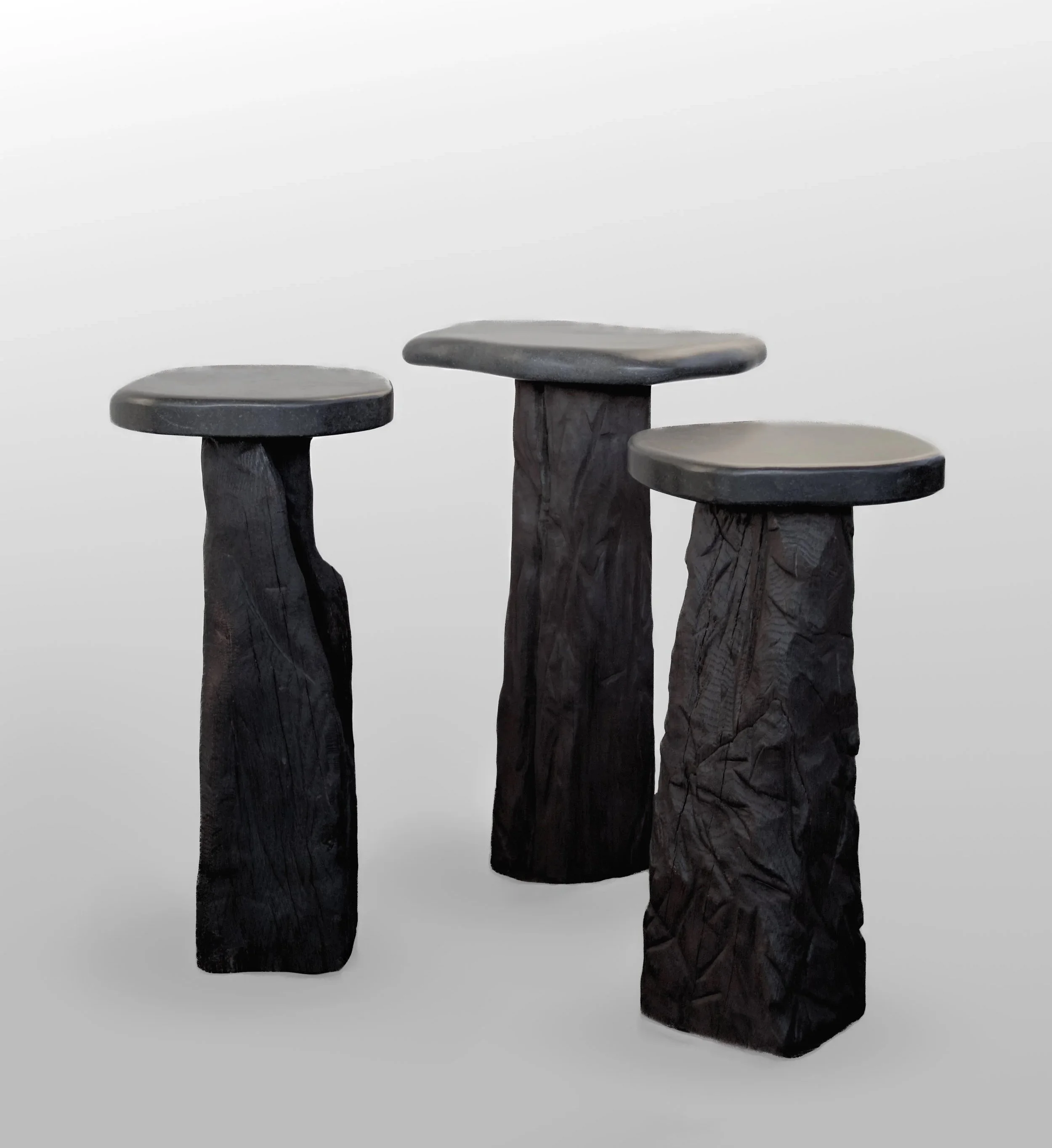Three black wooden stools with thick, round seats and textured, uneven bases, set against a plain white background.