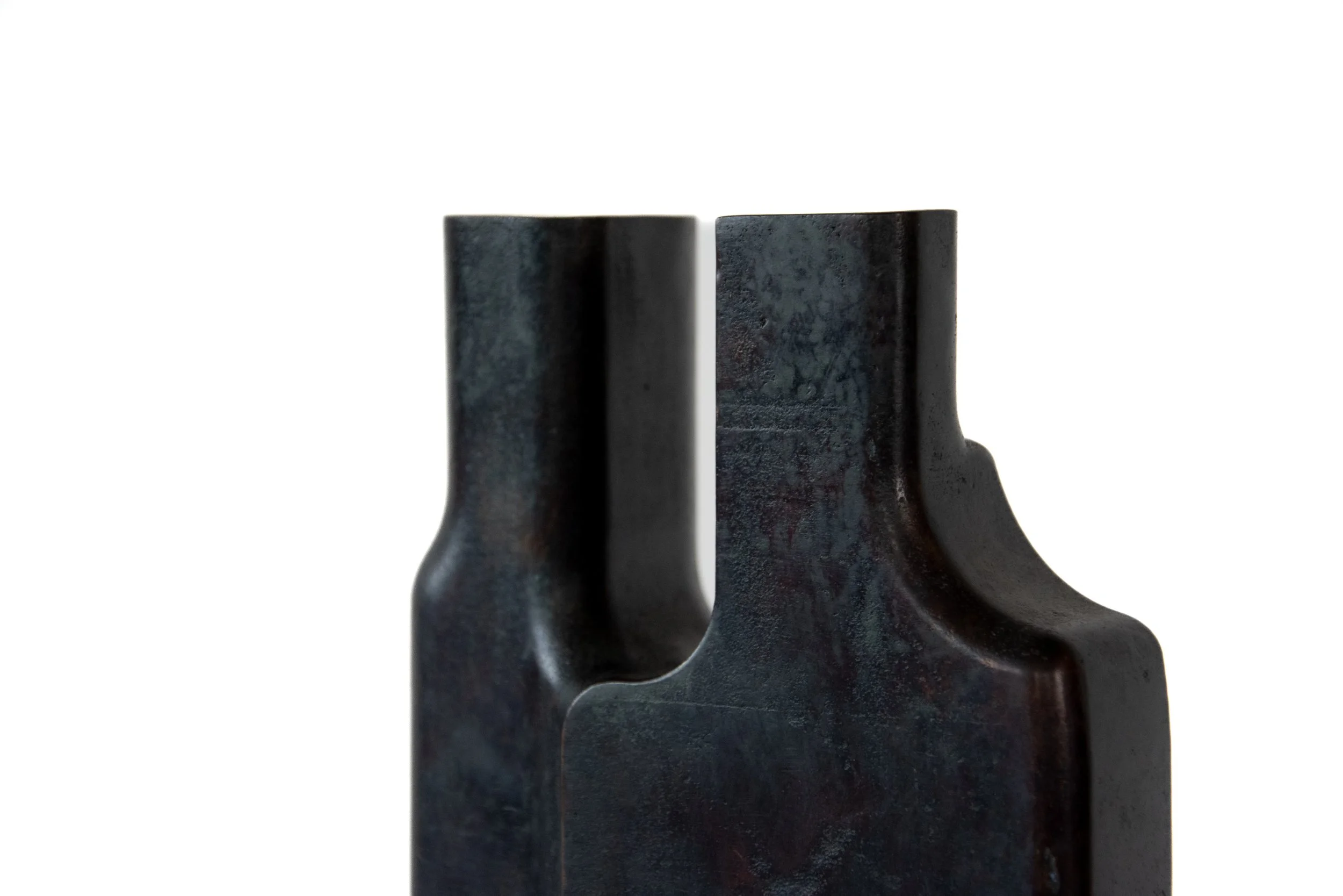 Close-up of two black, textured metal industrial components with curved and flat surfaces, against a plain white background.