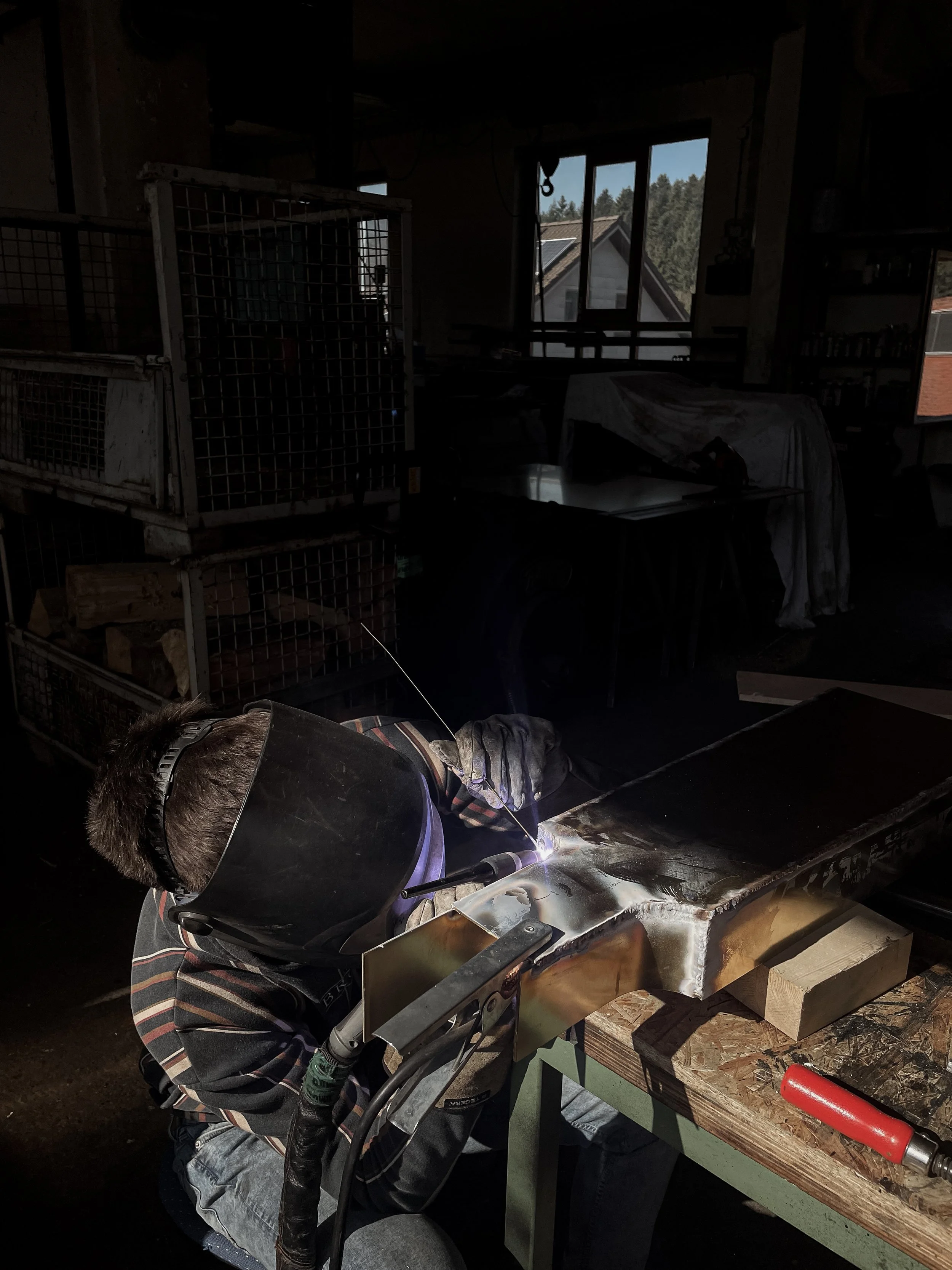 A person welding metal in a workshop, wearing a safety helmet and gloves, with sparks flying from the welding process.