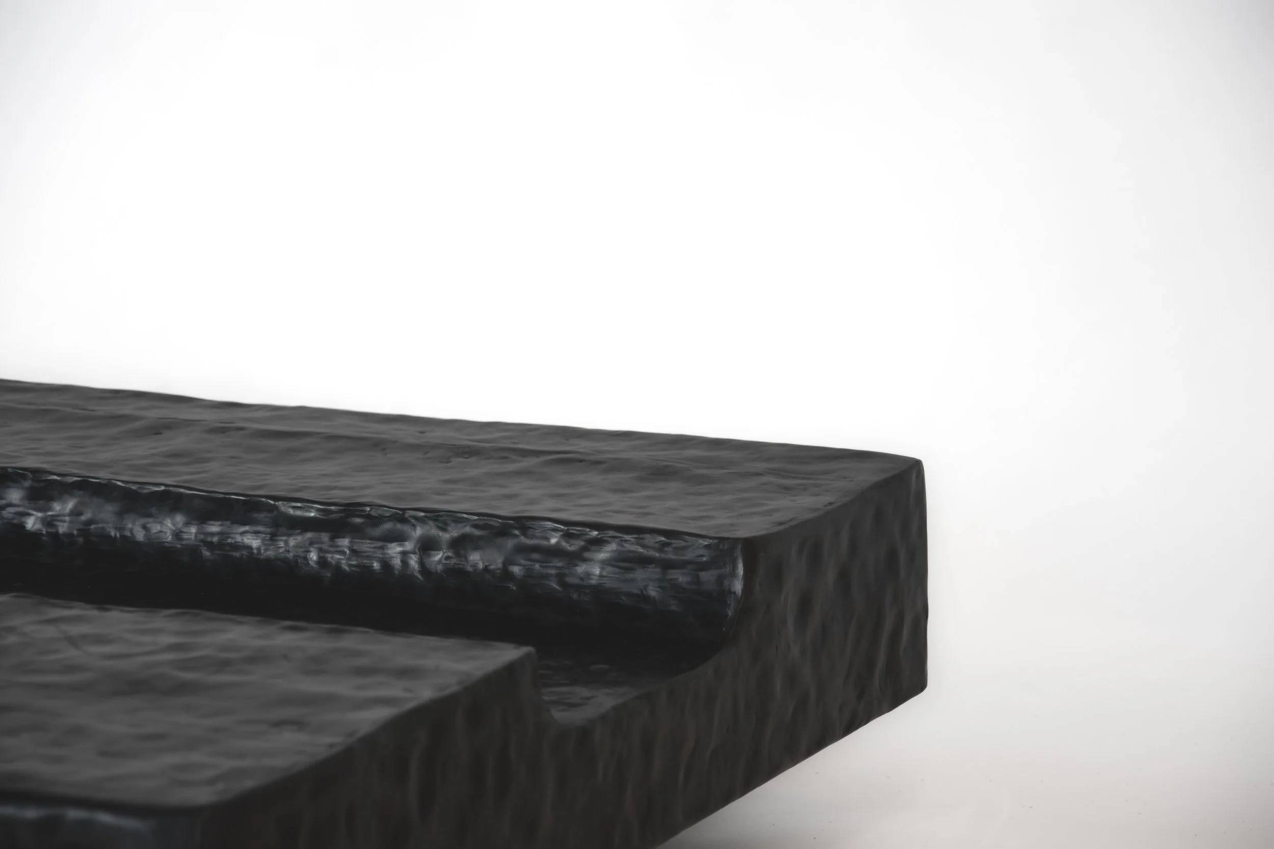 Close-up of a black metal sculpture with textured surface against a white background.