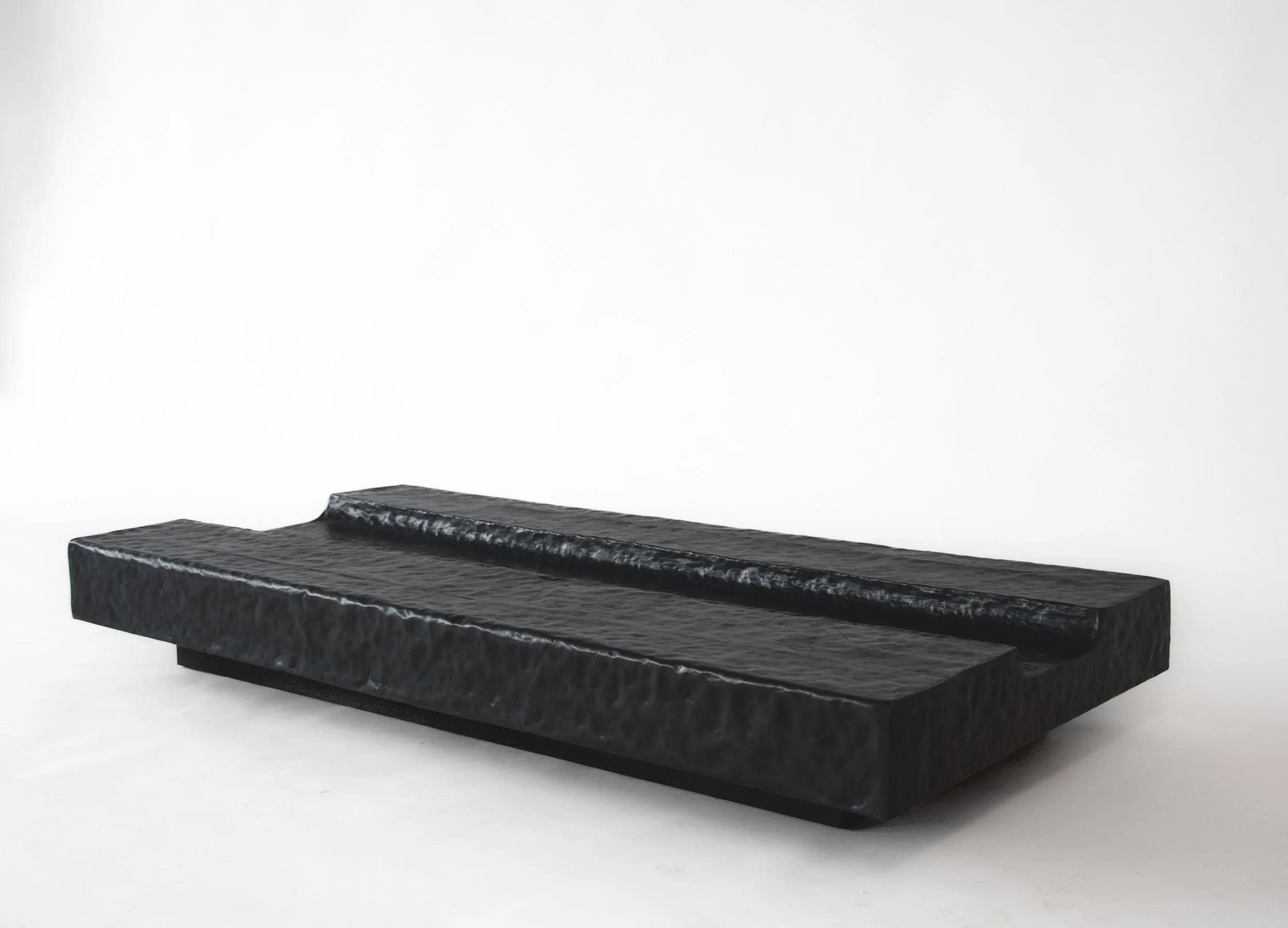 Black textured rectangular sculpture with a textured surface, displayed against a white background.