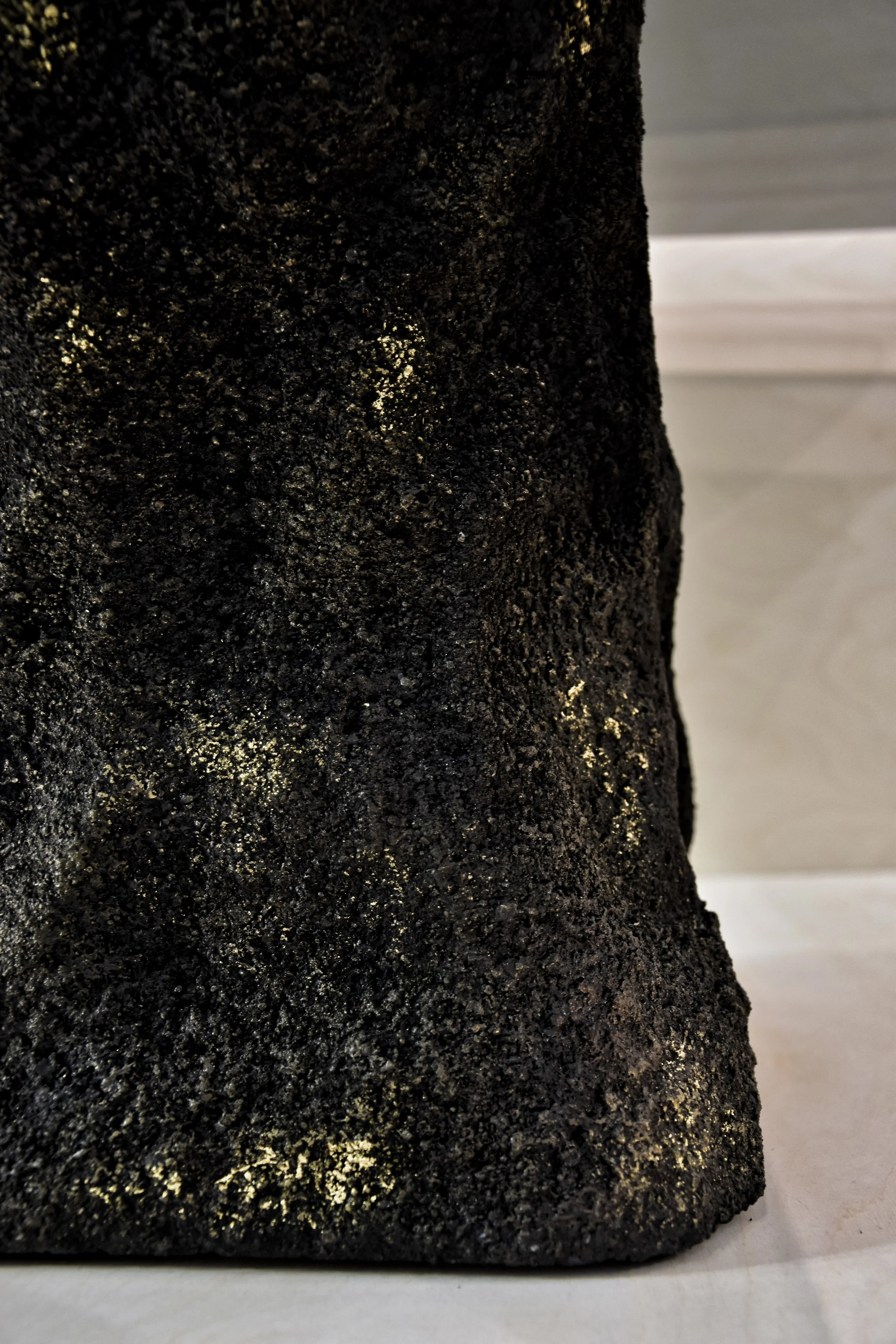 Close-up of a textured black material with gold specks on a white surface.