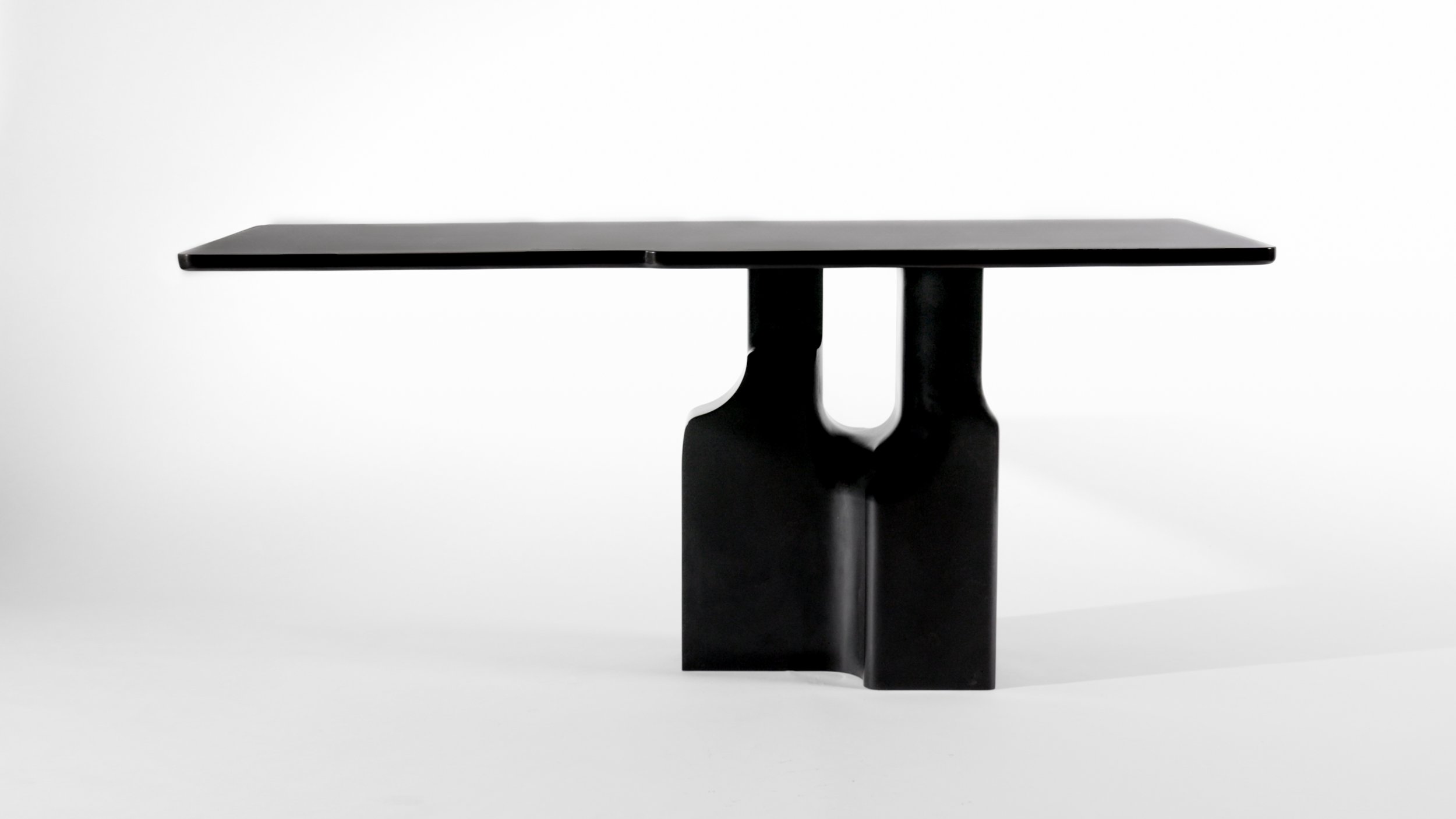Black modern table with a rectangular top and sculptural base, set against a plain white background.