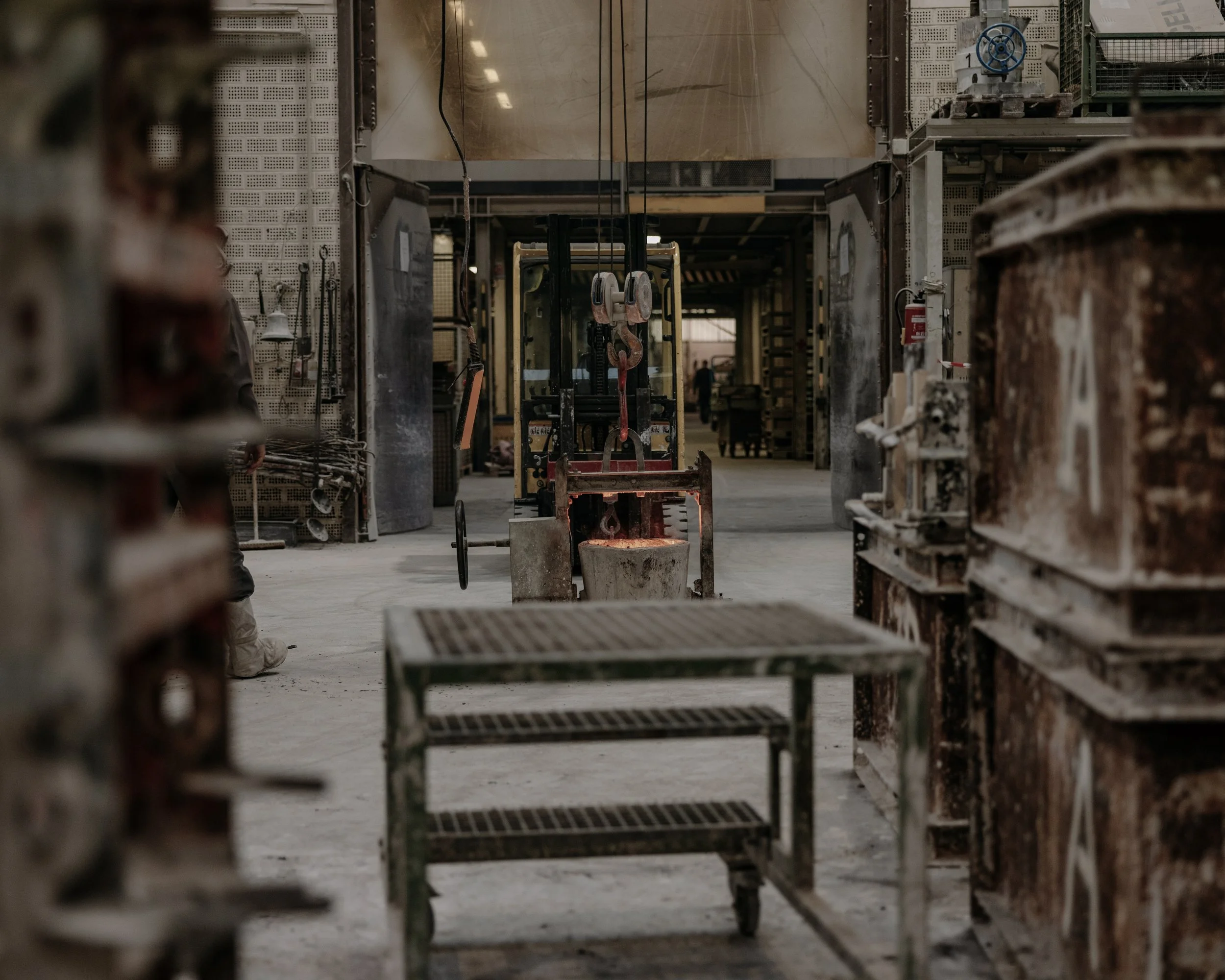 Industrial workshop with a furnace and various equipment, including a metal cart and storage shelves, in a maintenance or manufacturing environment.